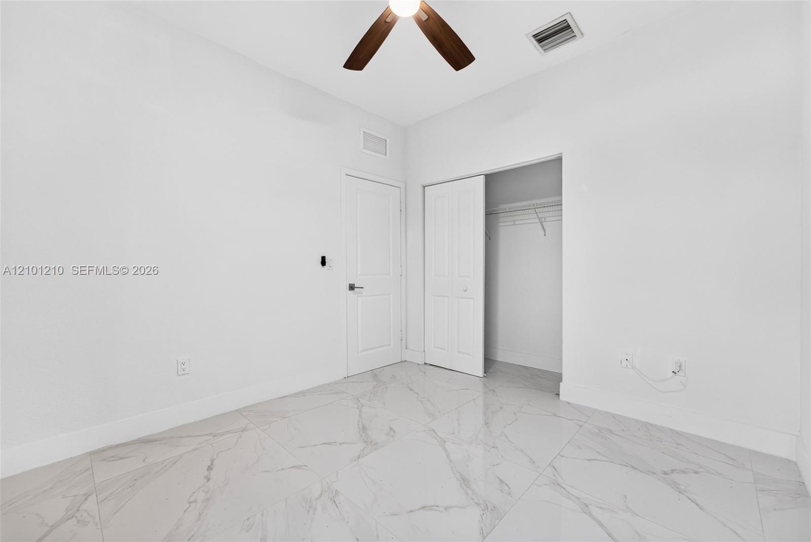 Unfurnished room with marble-look tile flooring, ceiling fan, and open closet.