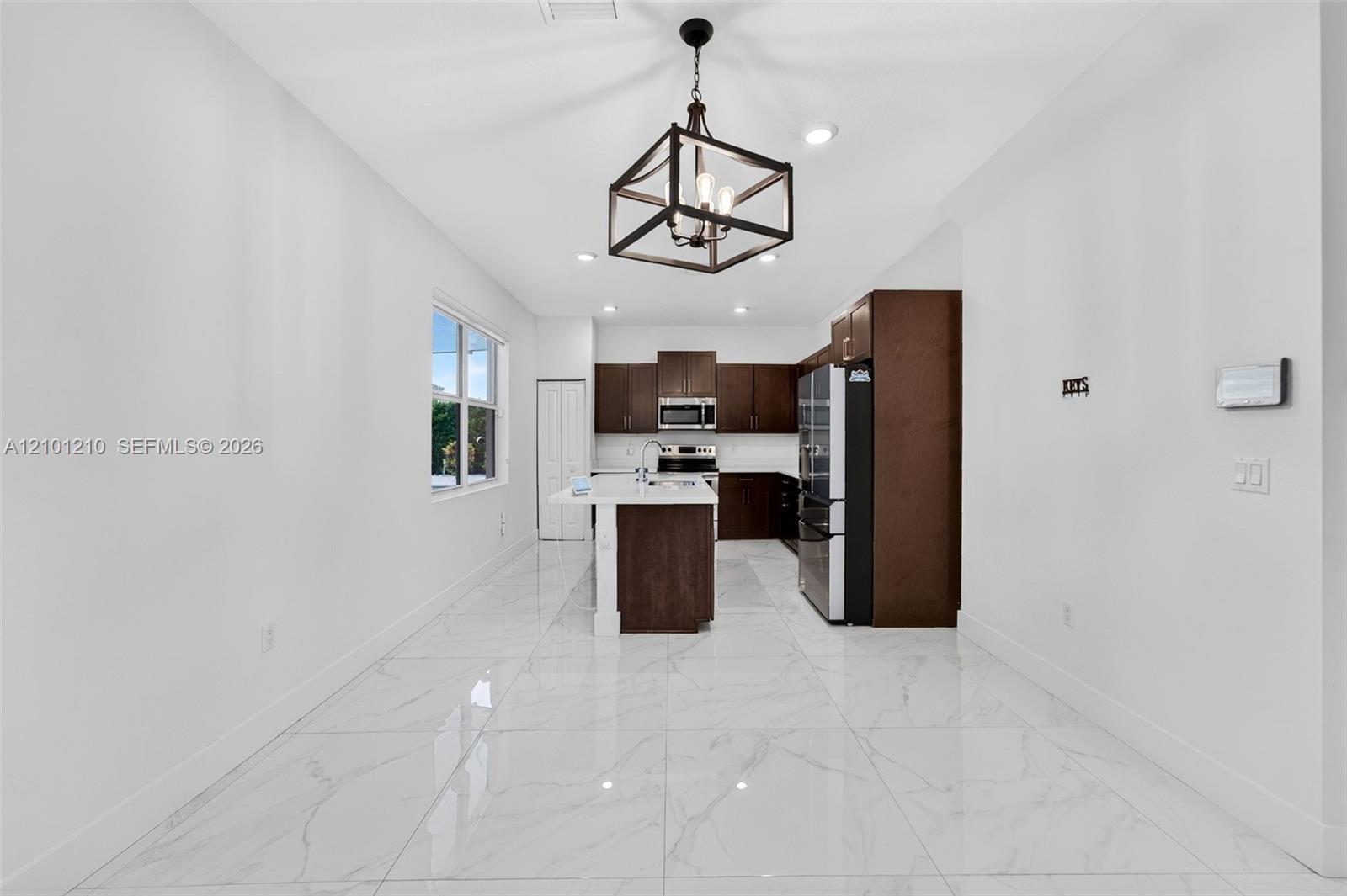 Unfurnished kitchen with dark wood cabinets, a white island, stainless appliances, and glossy tile floors.
