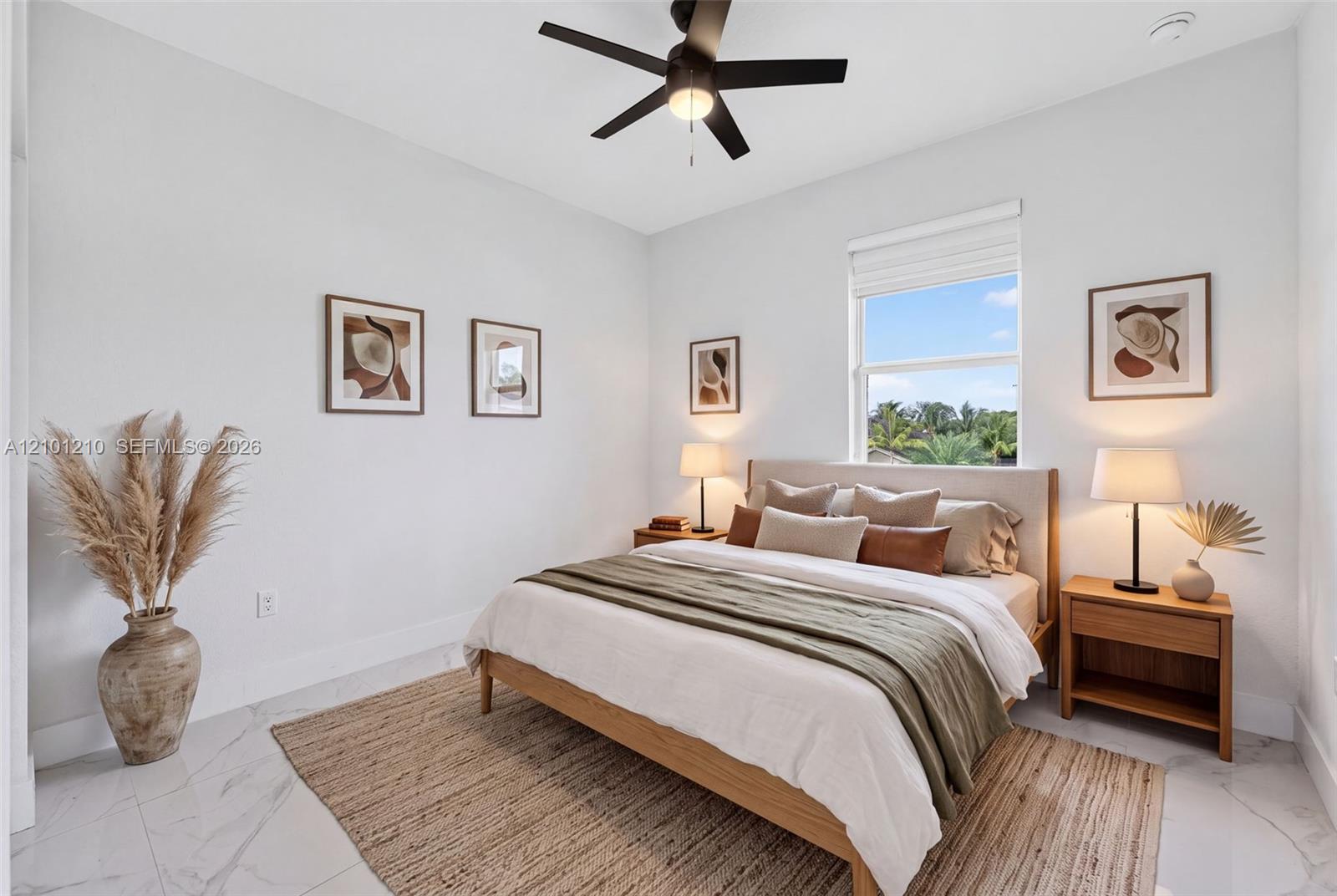 Staged bedroom with a wood bed, marble-look tile floor, and a window overlooking palm trees.