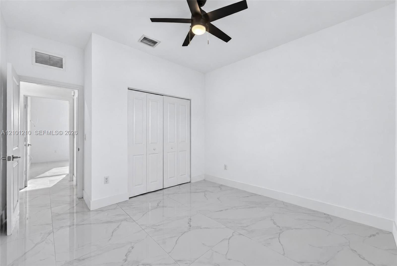 Empty bedroom with a black ceiling fan, white closet doors, and glossy gray-veined tile flooring.