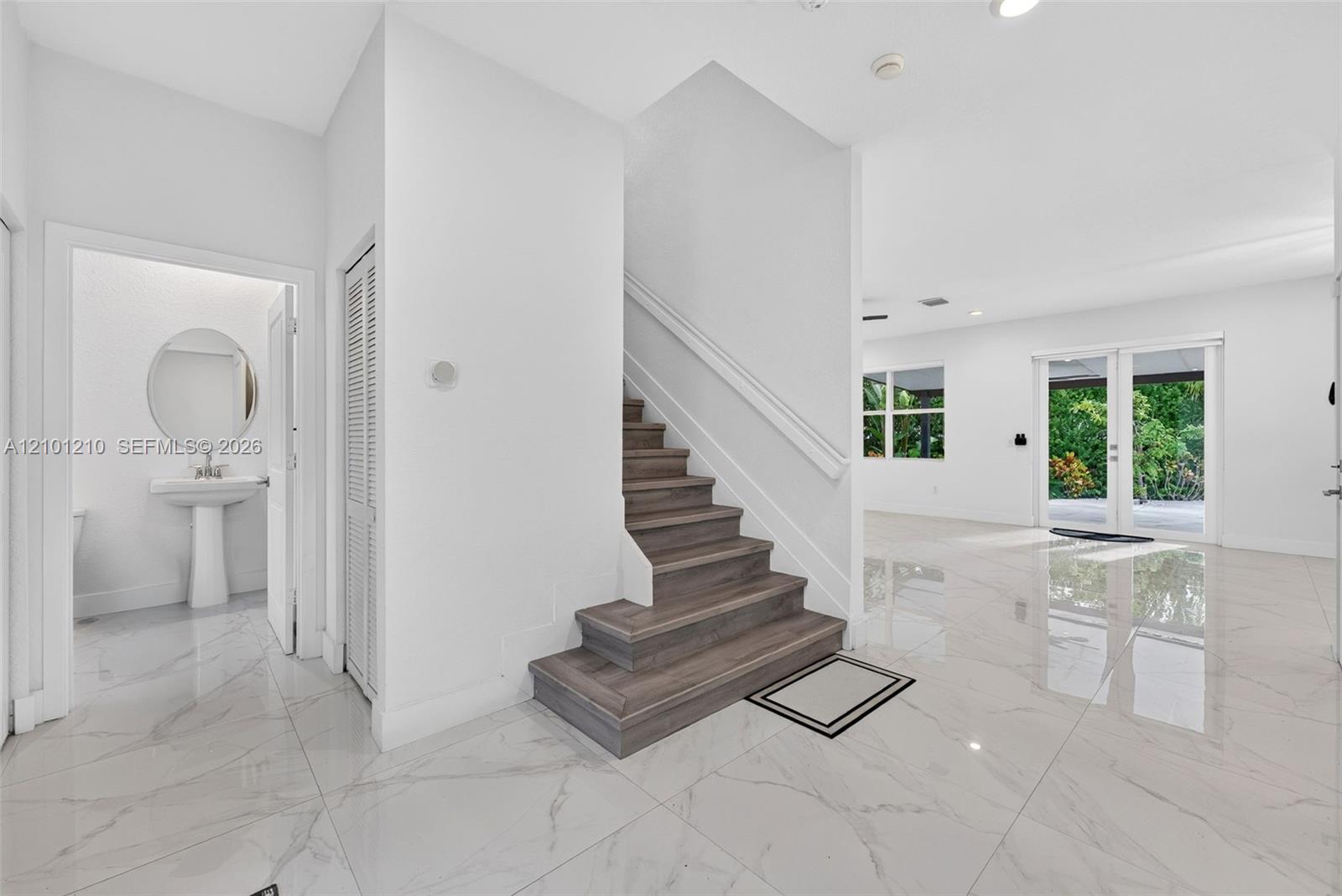 Foyer with a dark wood staircase, glossy tile floors, and sliding glass doors opening to greenery.