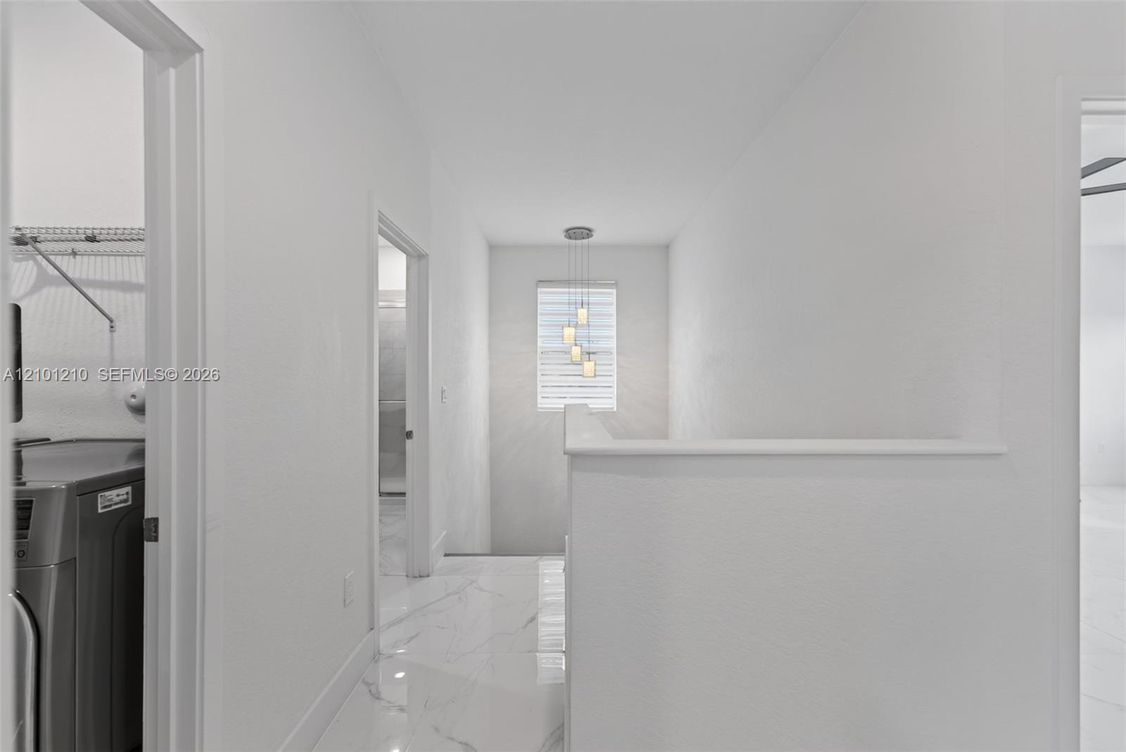 White hallway with glossy marble-look floors, pendant lights, and a laundry area through the left doorway.