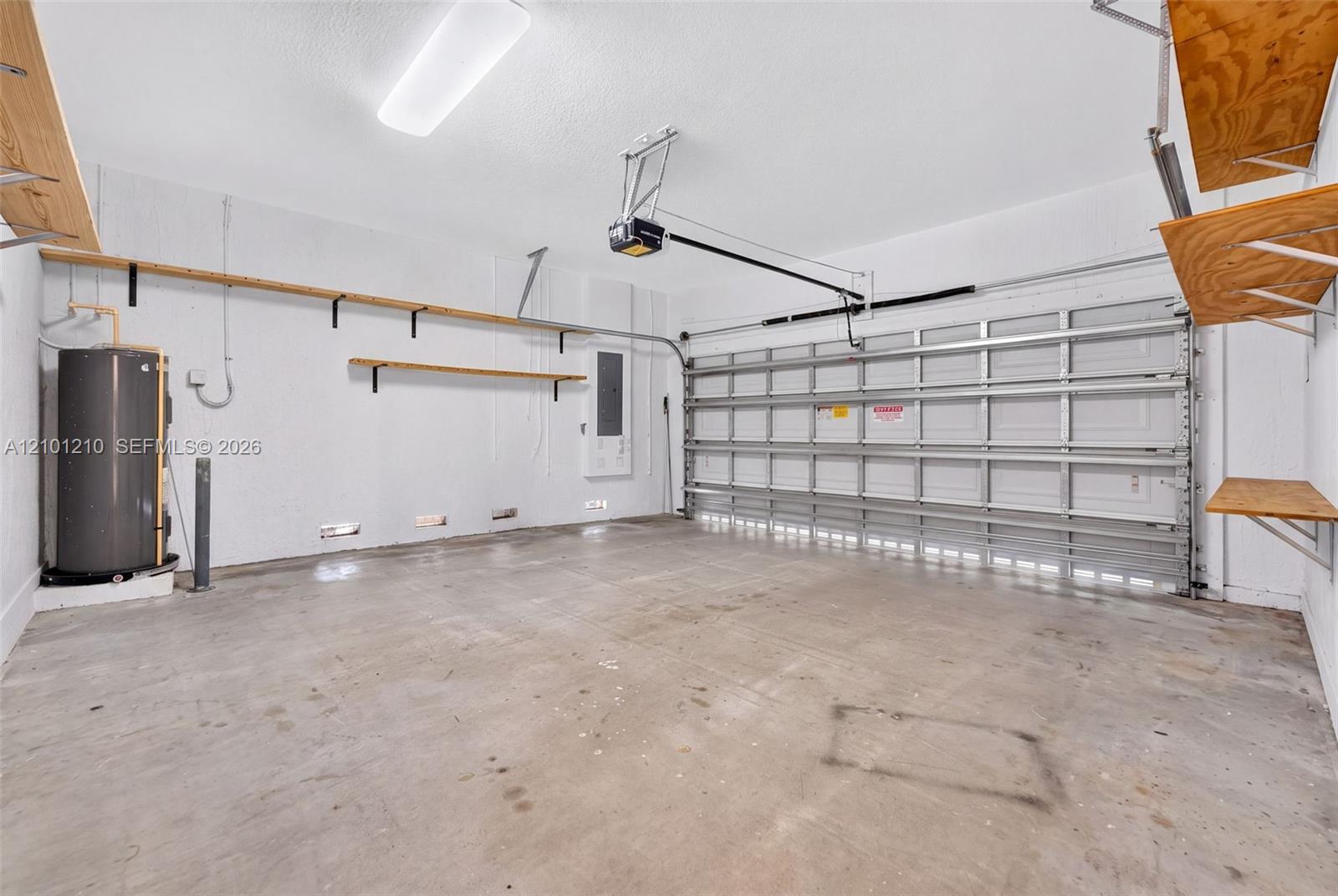 Empty garage with a concrete floor, wall shelving, water heater, and closed sectional garage door.