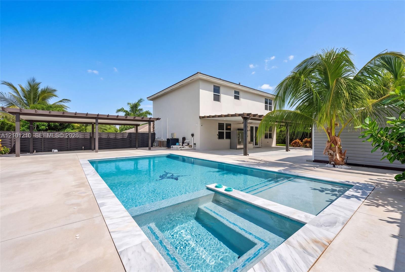Backyard swimming pool with a shallow sun shelf beside a two-story home and covered patio.
