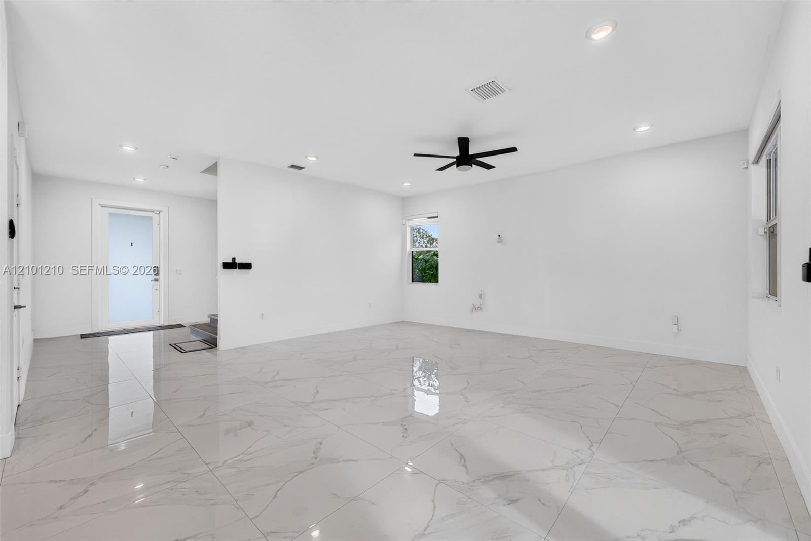 Vacant living room with glossy marble-look tile floors, white walls, and a black ceiling fan.
