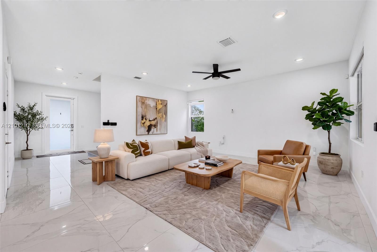 Staged living room with a white sectional, tan chairs, glossy tile floors, and a black ceiling fan.