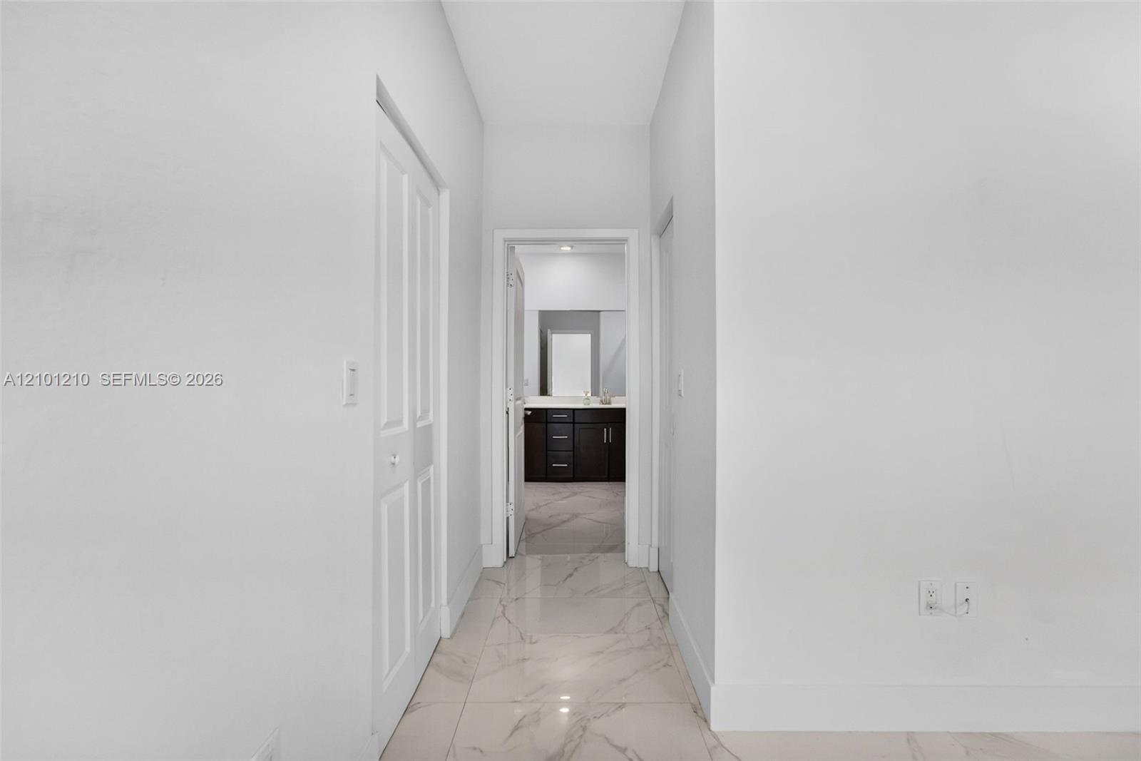 Interior hallway with glossy marble-look floors leading to a bathroom with a dark vanity.