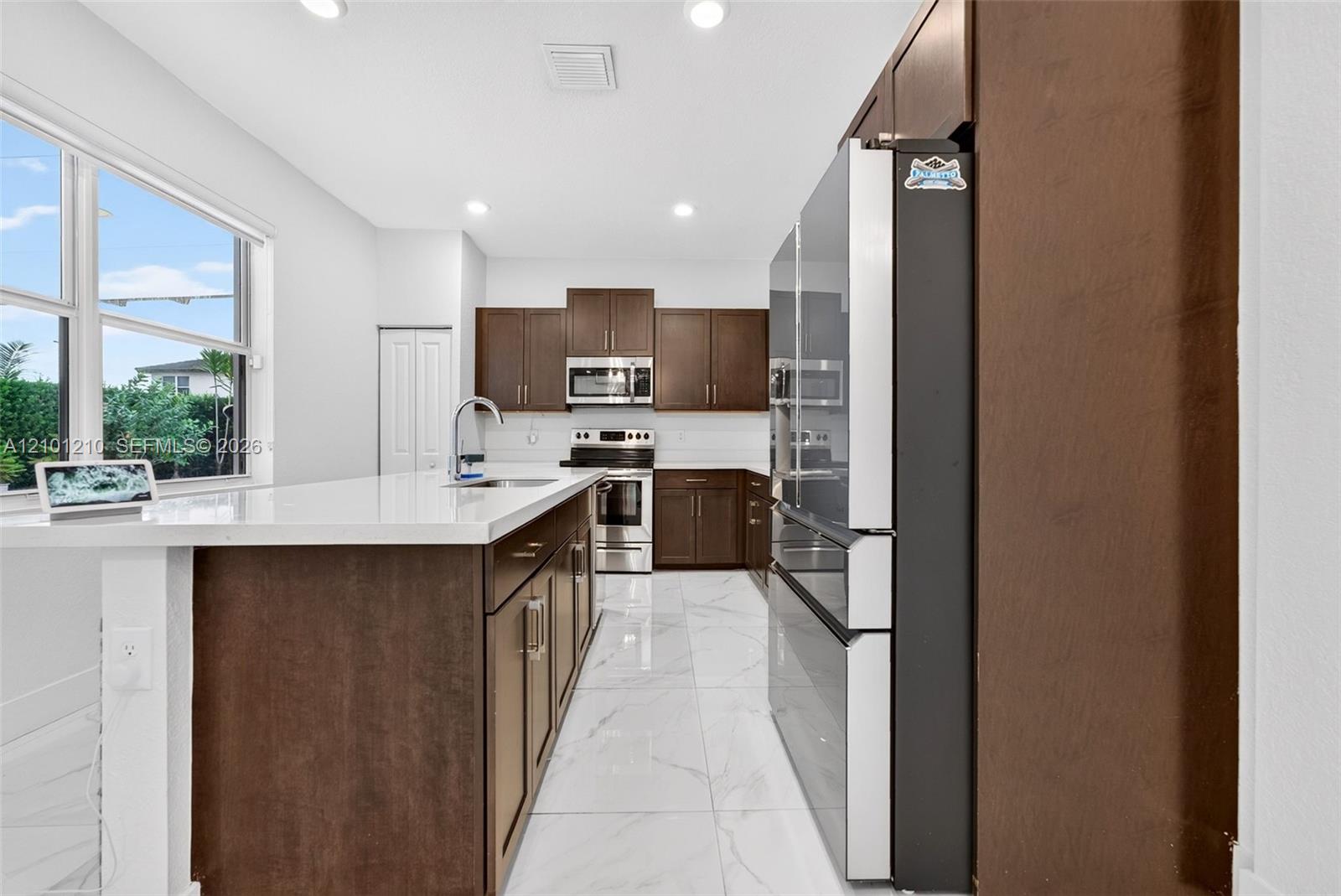 Kitchen with dark wood cabinets, a white island, stainless steel appliances, and large windows.