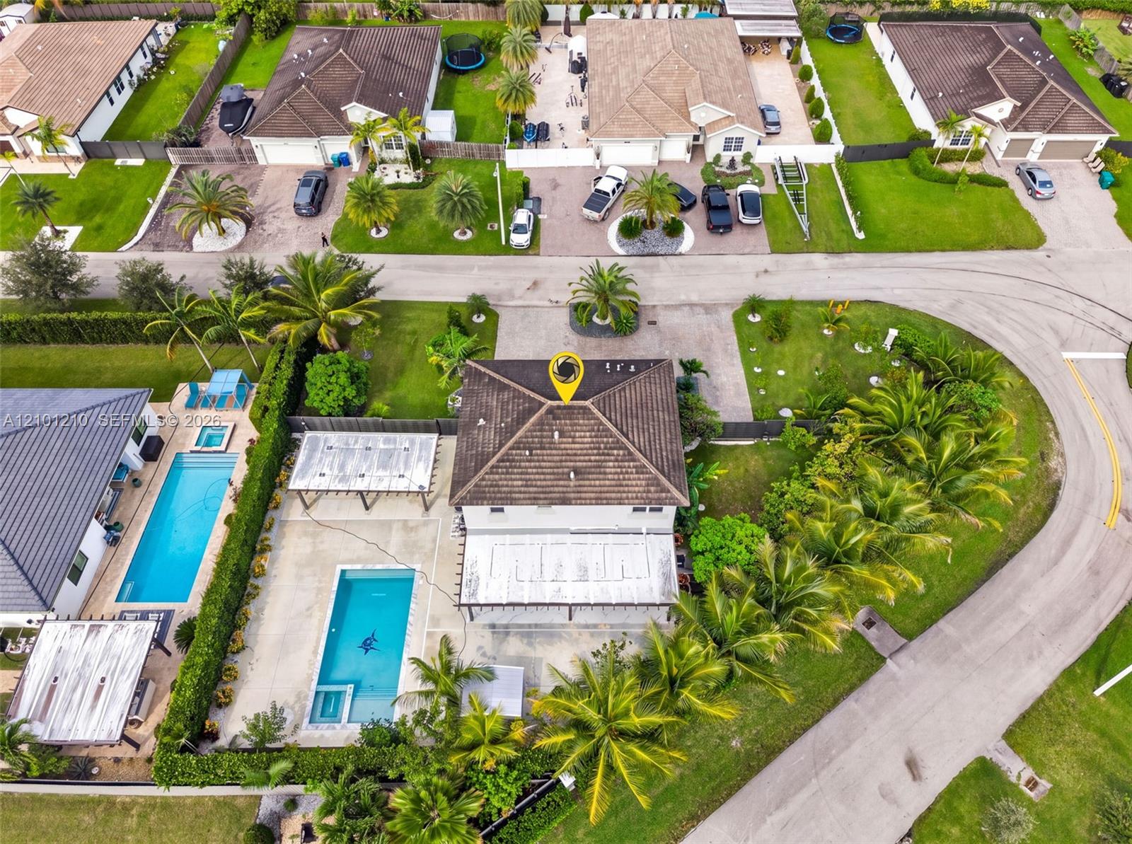 Aerial view of a Miami home with a tiled roof, palm-lined yard, and backyard pool.