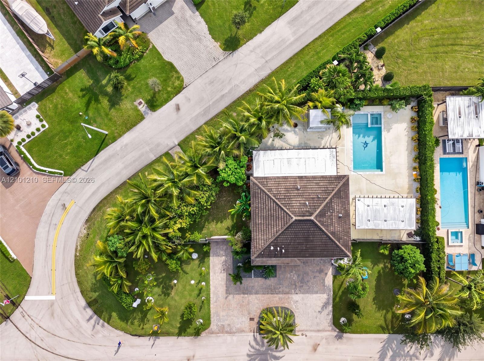 Aerial view of a landscaped home with a swimming pool beside a curved residential street.