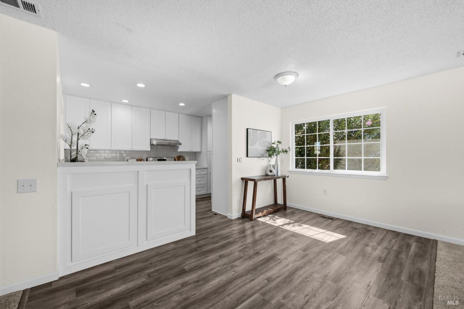 Open kitchen and dining area with white cabinetry, gray plank floors, and a sunlit window.