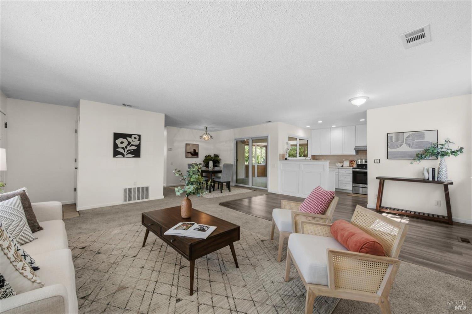 Staged open-plan living room with a patterned rug, dining area, and white kitchen.