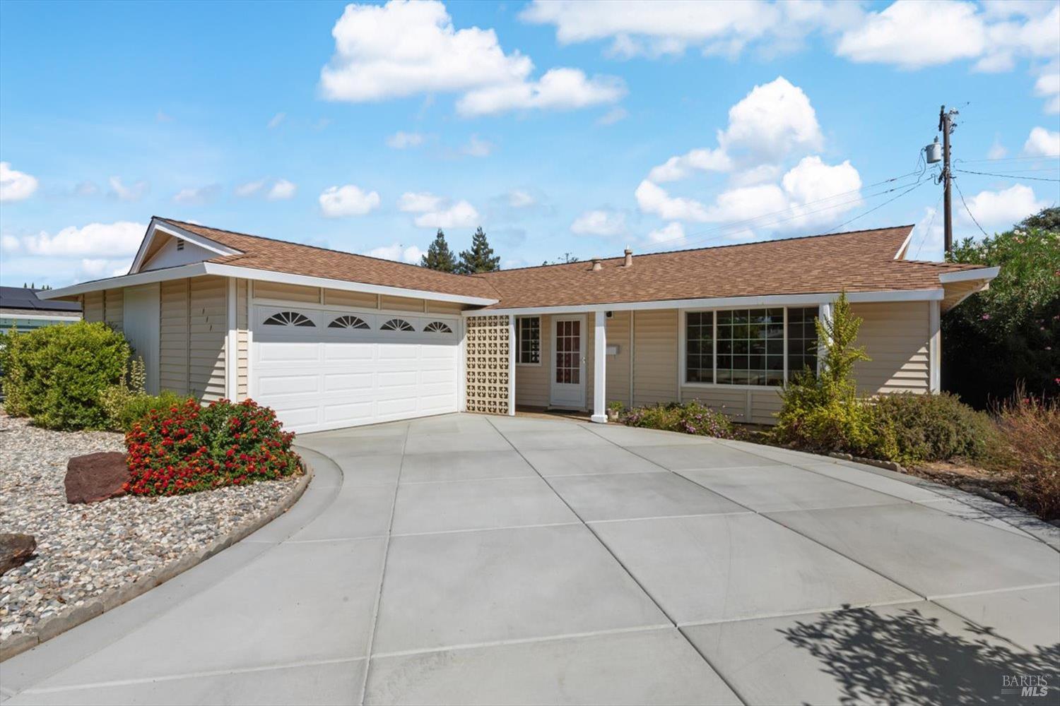 Single-story beige home with a white double garage door and landscaped driveway.