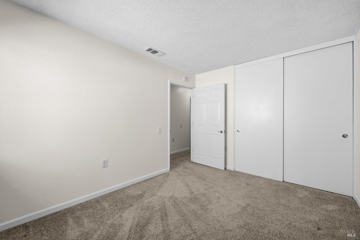 Empty bedroom with beige carpet and large white sliding closet doors.