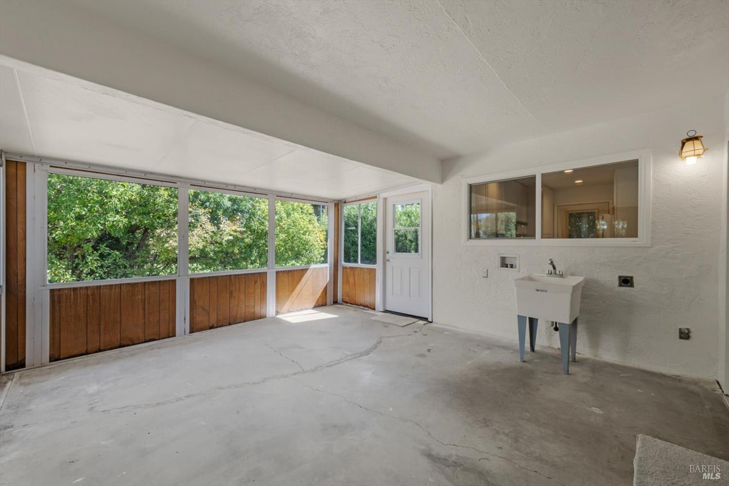 Enclosed sunroom with a wall of windows, wood-paneled lower walls, and a utility sink.