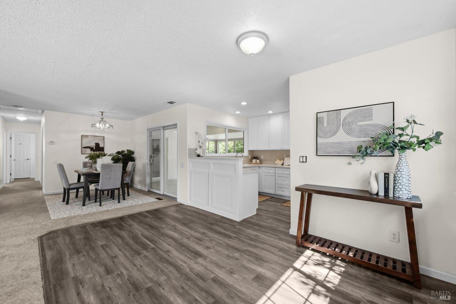 Open-plan dining area and white kitchen with a peninsula and wood-look flooring.