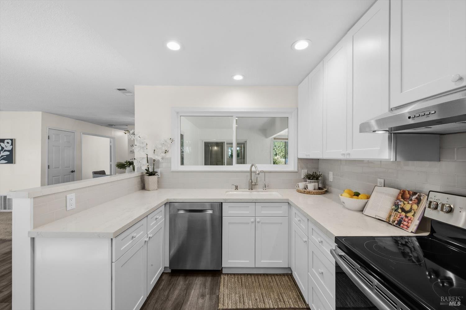 Bright white kitchen with a pass-through window, peninsula, stainless steel dishwasher, and black range.