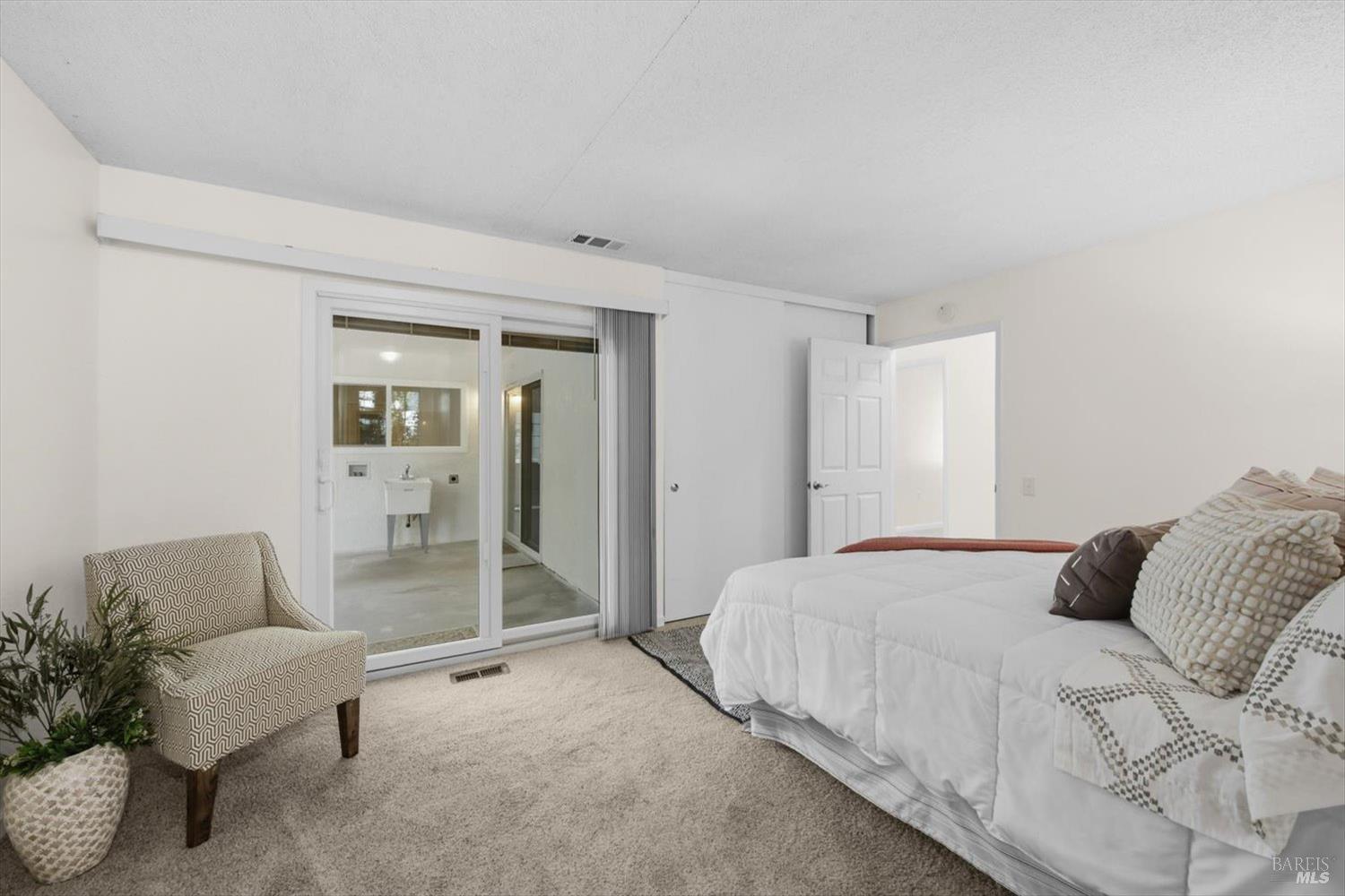 Bedroom with a white-covered bed, patterned chair, and sliding glass doors to a bathroom.