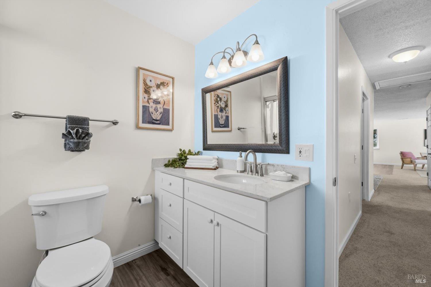 Bathroom with white vanity and toilet, blue accent wall, and an open hallway.