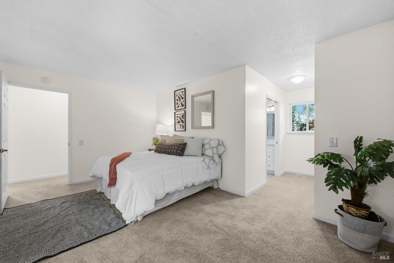 Staged bedroom with a white bed, rust-colored throw, and patterned rug.