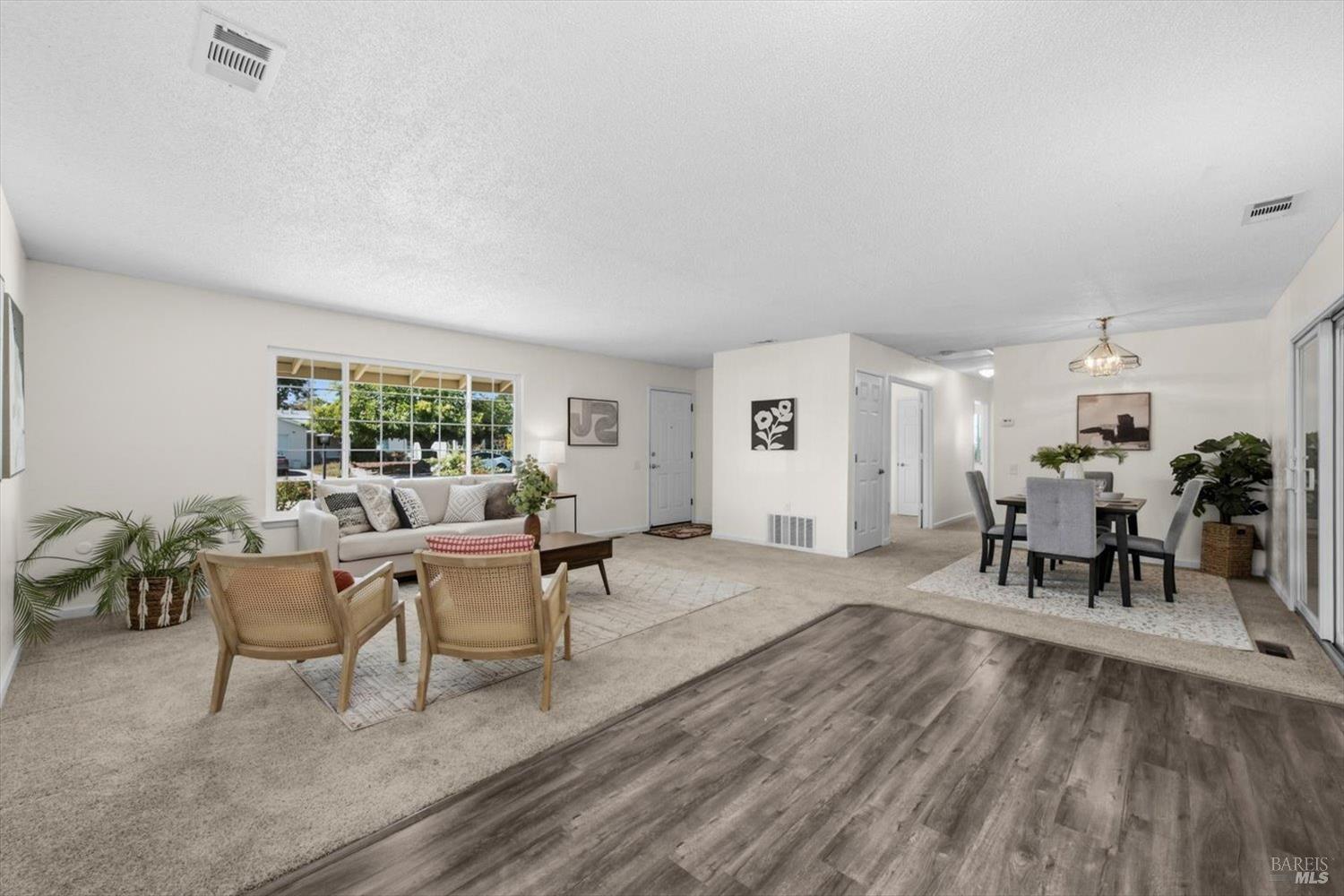 Open-plan living and dining room with neutral furnishings, a large window, and gray wood-look flooring.