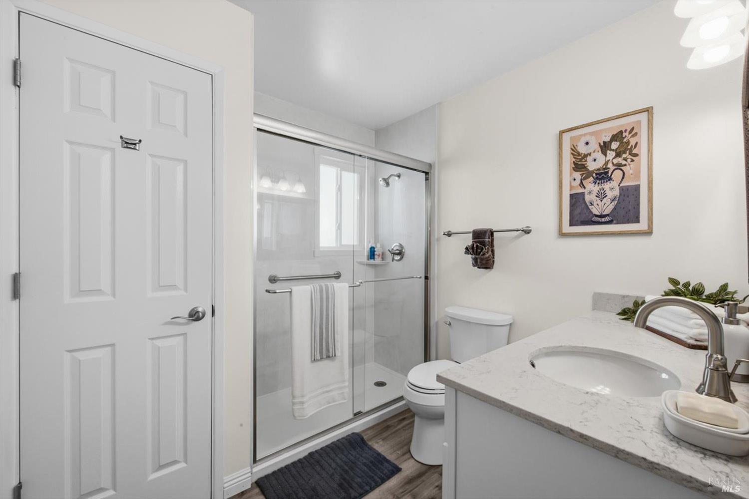Bathroom with glass-enclosed shower and white vanity topped with a marble-look counter.