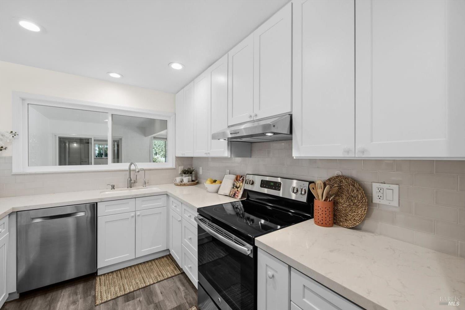 Bright kitchen with white shaker cabinets, pale stone counters, and a black glass-top range.