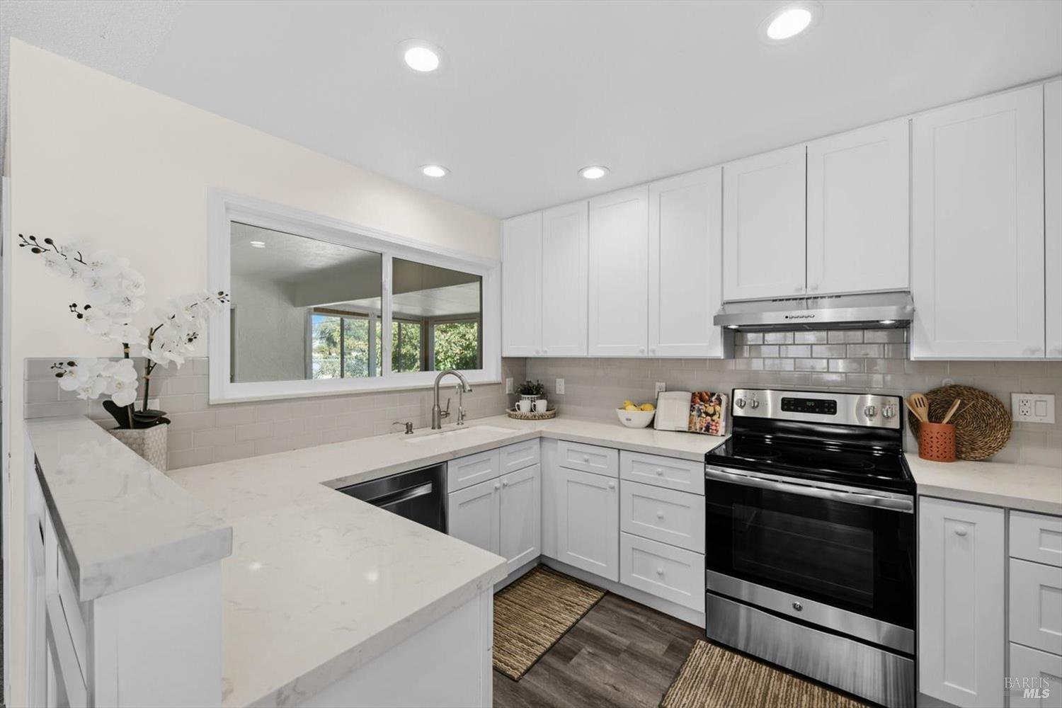 Renovated white kitchen with marble-look counters, a pass-through window, and a black-and-stainless range.