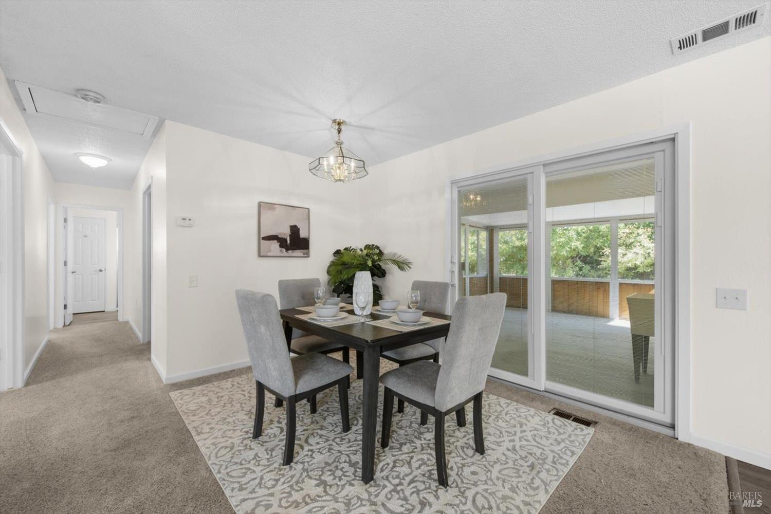 Dining room with a dark table and gray chairs beside sliding doors to a bright sunroom.