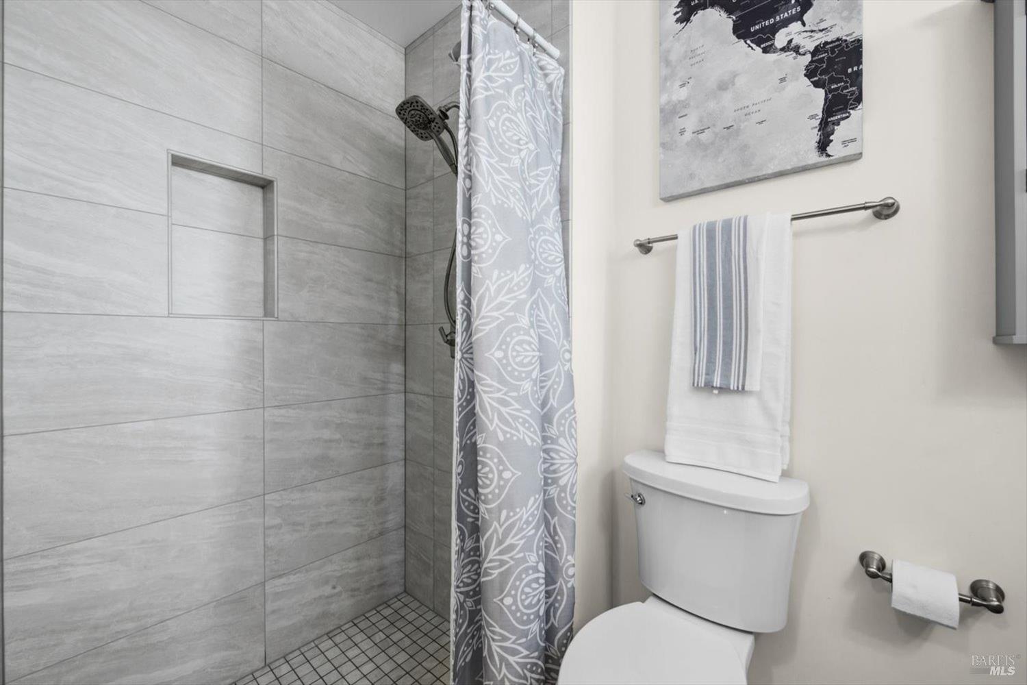 Bathroom with a gray-tiled shower, recessed niche, patterned curtain, and white toilet.