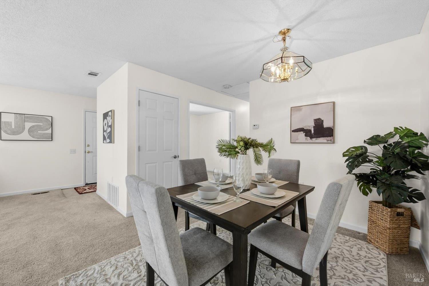 Dining area with a set table, gray chairs, chandelier, and large potted plant.