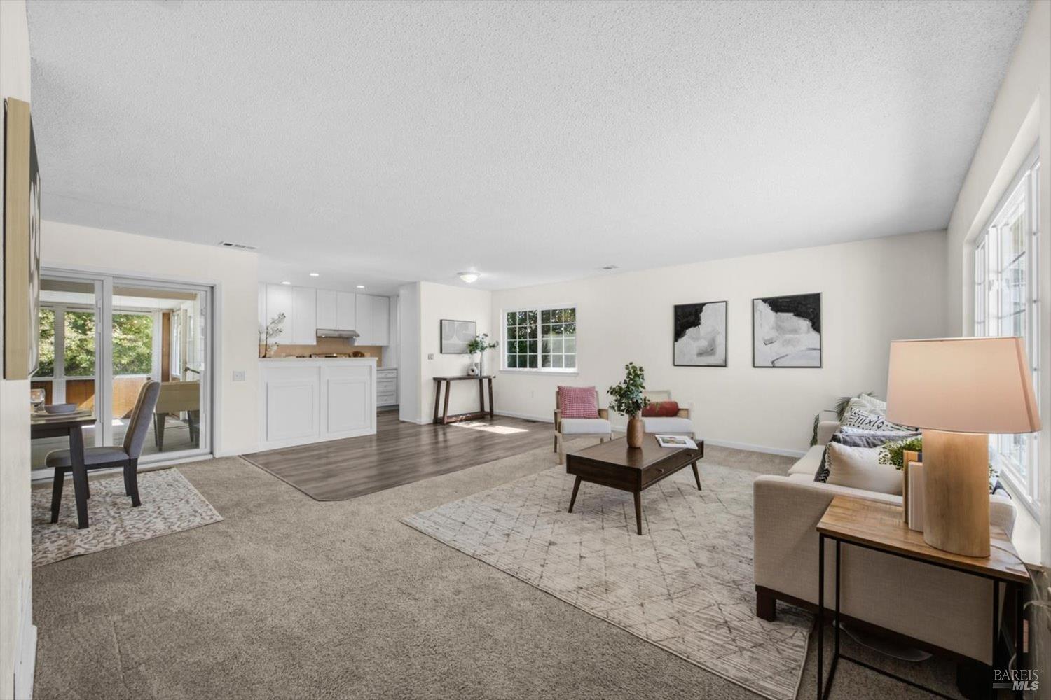 Open-plan living room with a white kitchen, dining area, and large windows.