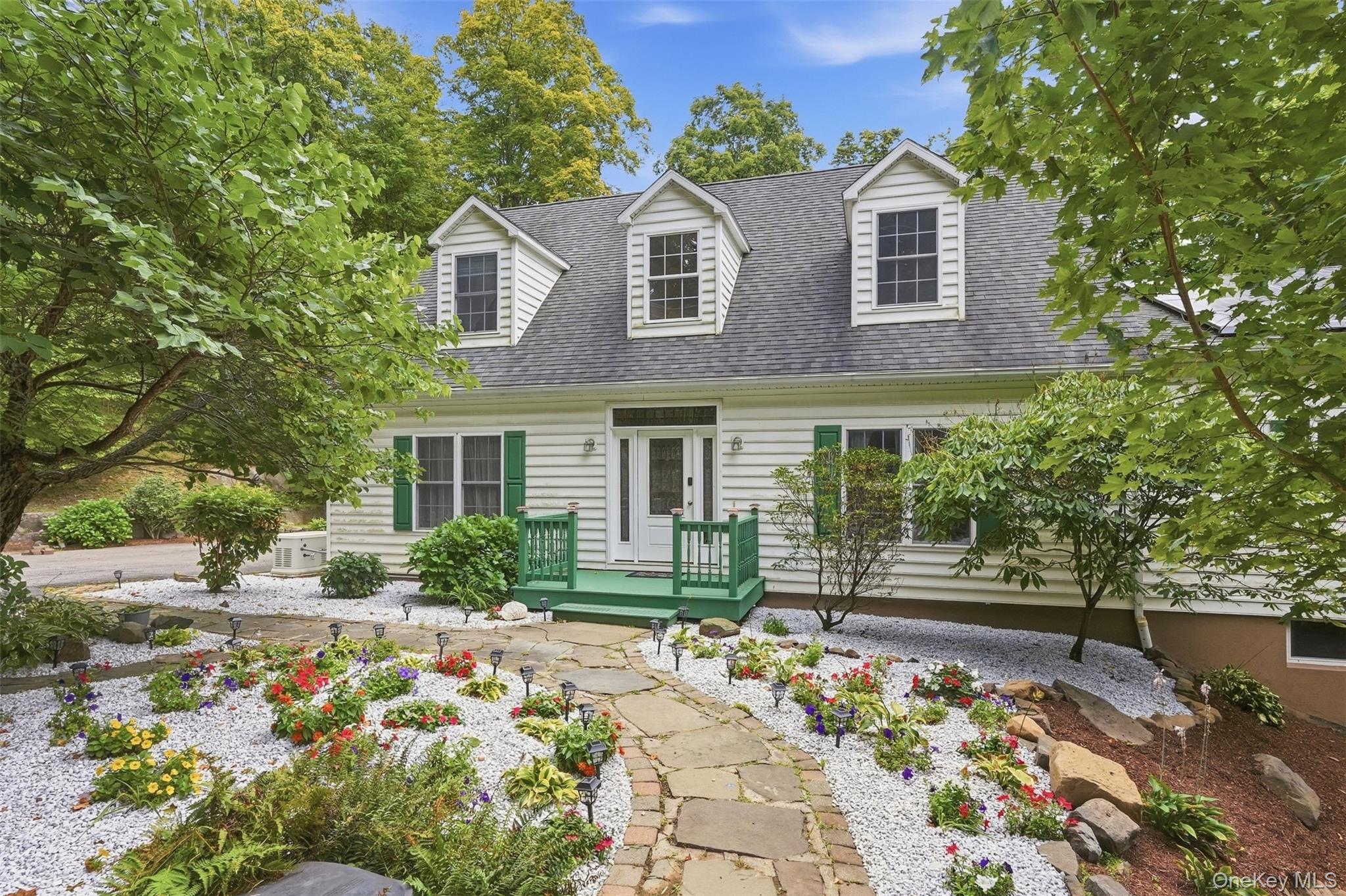 White house with three dormers, green porch, and a flower-lined stone path.