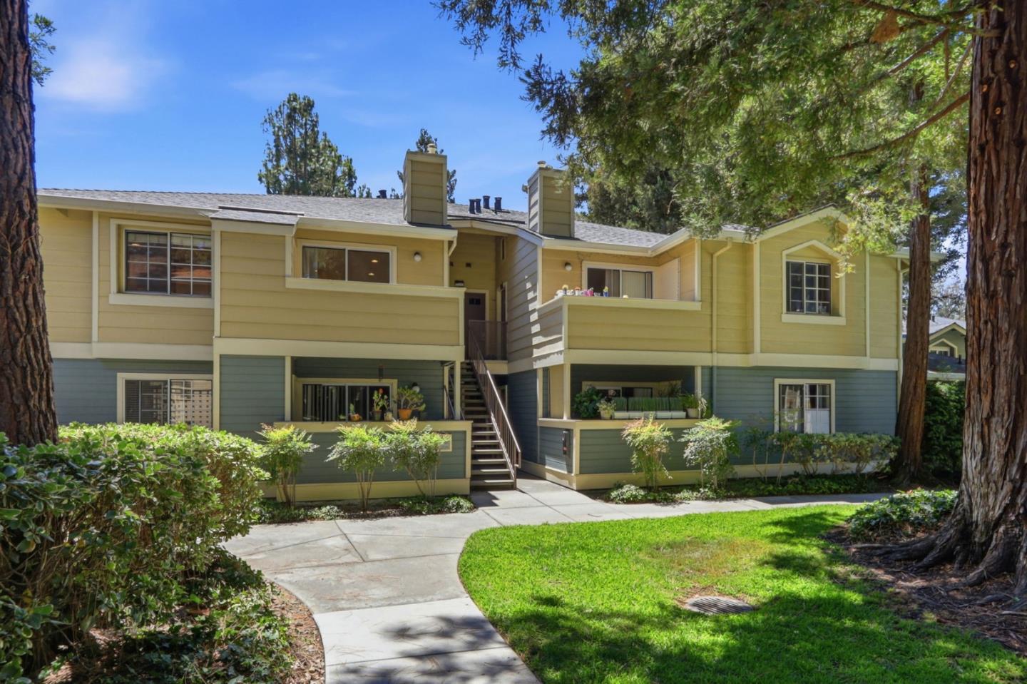 Two-story yellow and blue-gray residence with a central staircase, mature trees, and landscaped lawn.