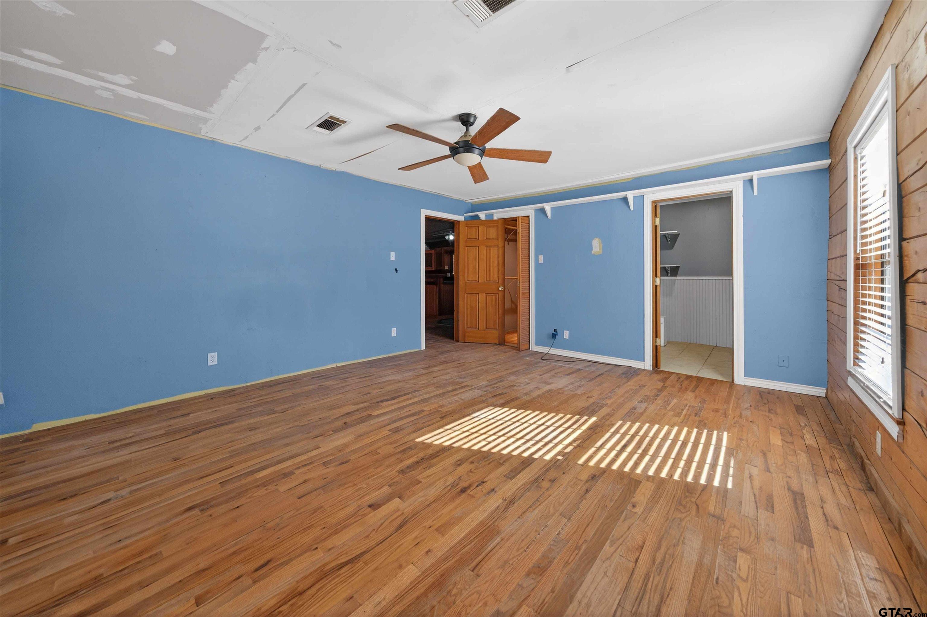 Vacant blue-walled room with hardwood floors, a ceiling fan, and an unfinished ceiling.