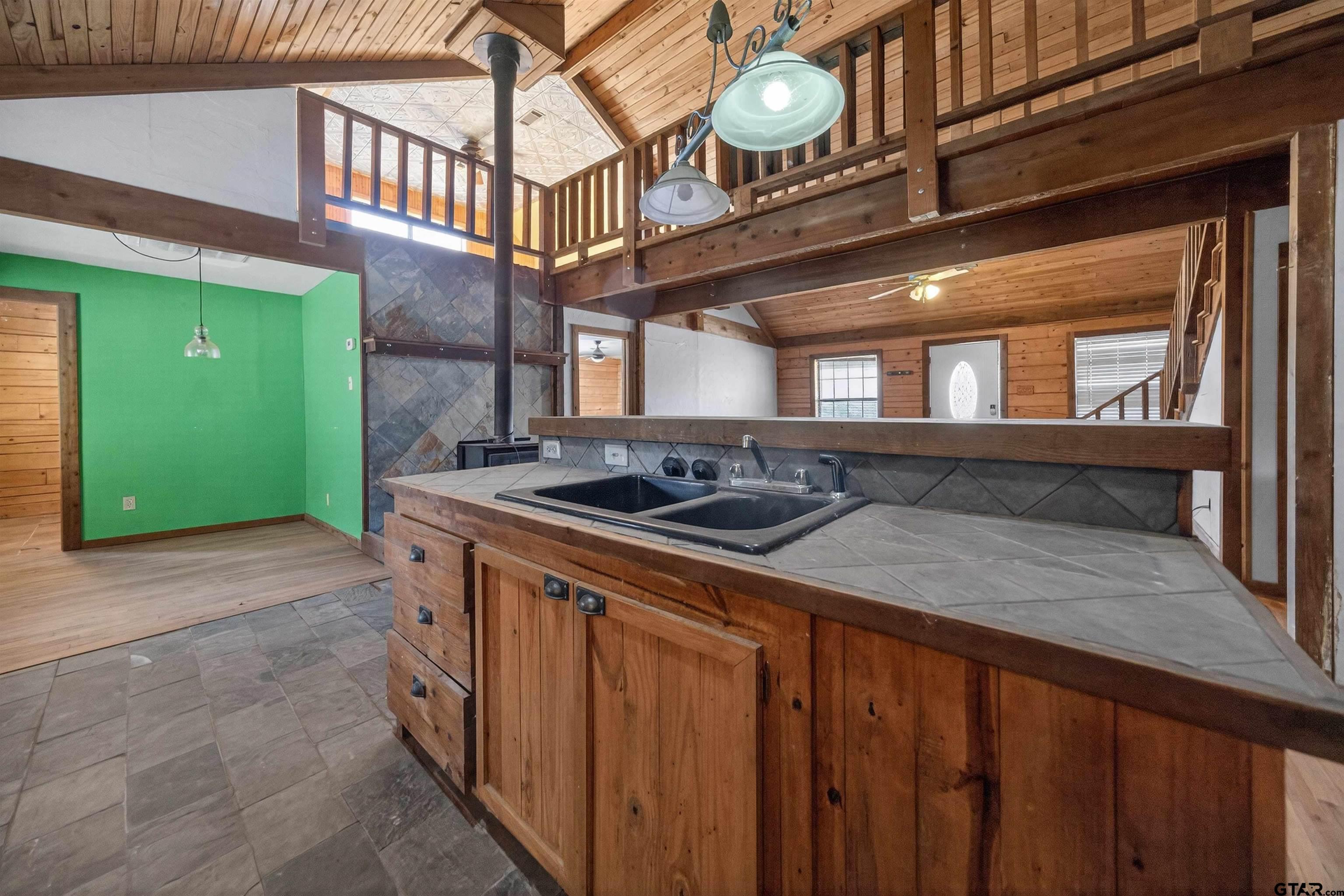 Rustic kitchen with a double-sink peninsula, wood-burning stove, and open loft above.