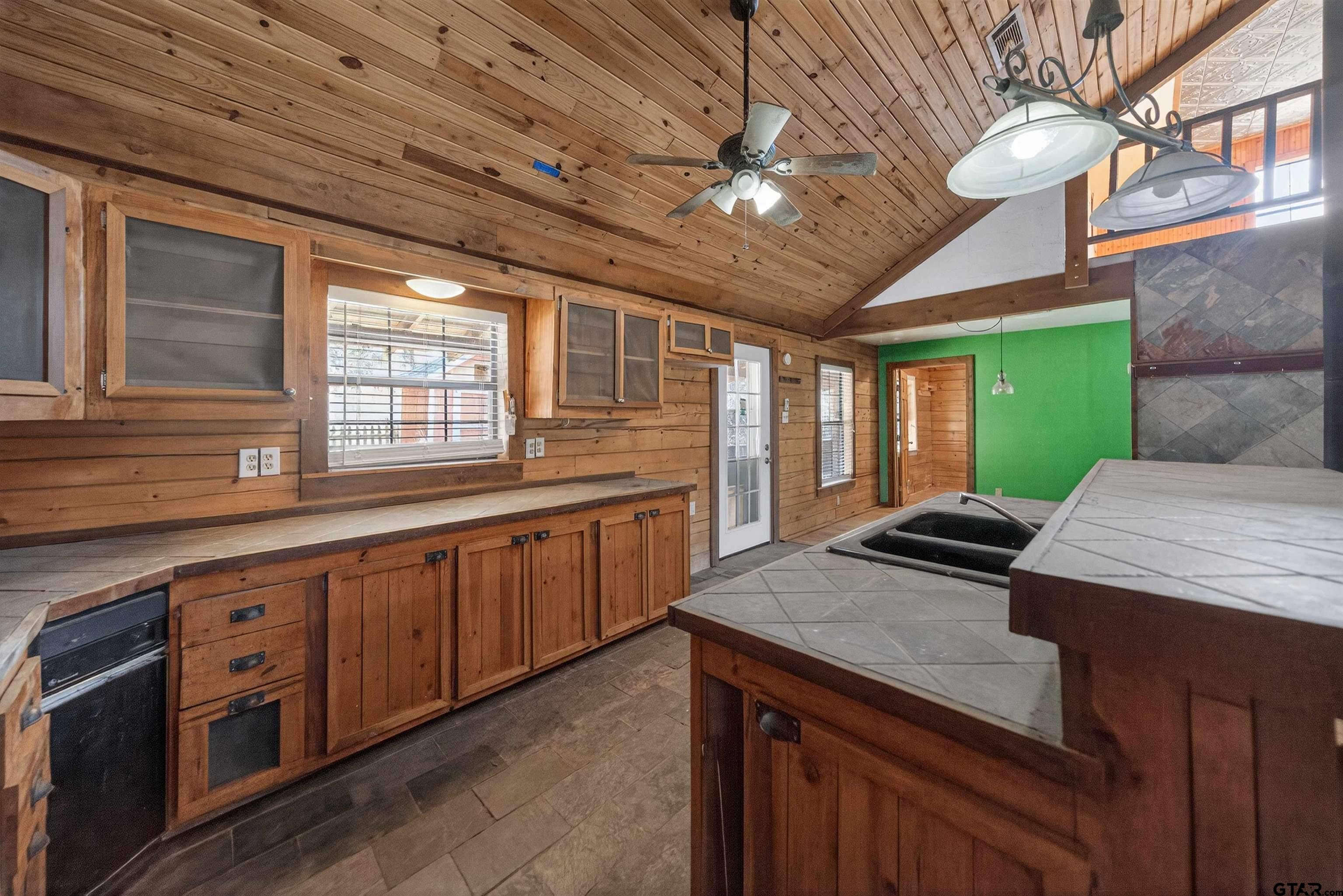 Kitchen with knotty wood cabinets, a sloped wood ceiling, tile counters, and a green accent wall.