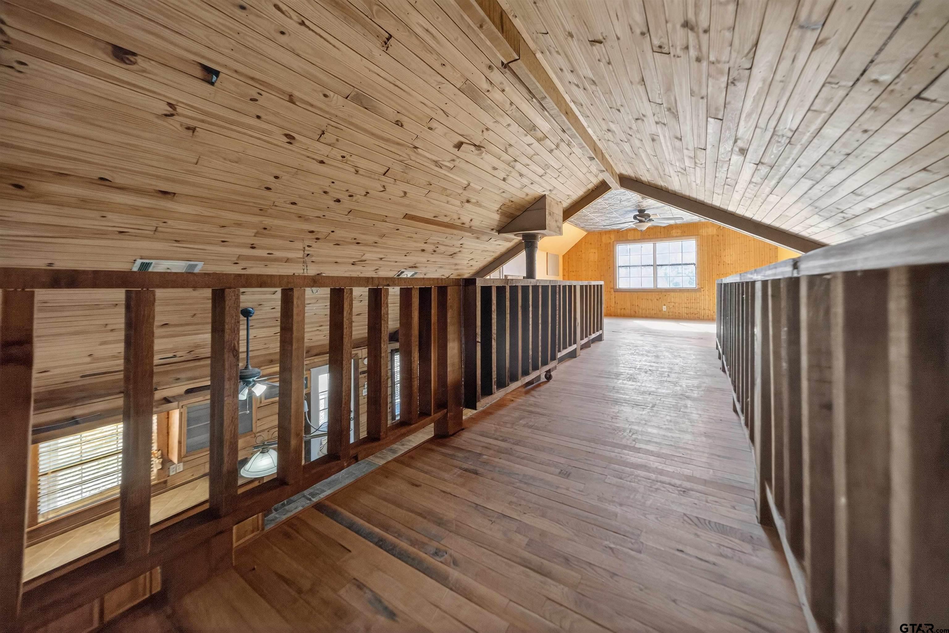 Wood-paneled loft landing with sloped ceiling, dark railings, and a large end window.