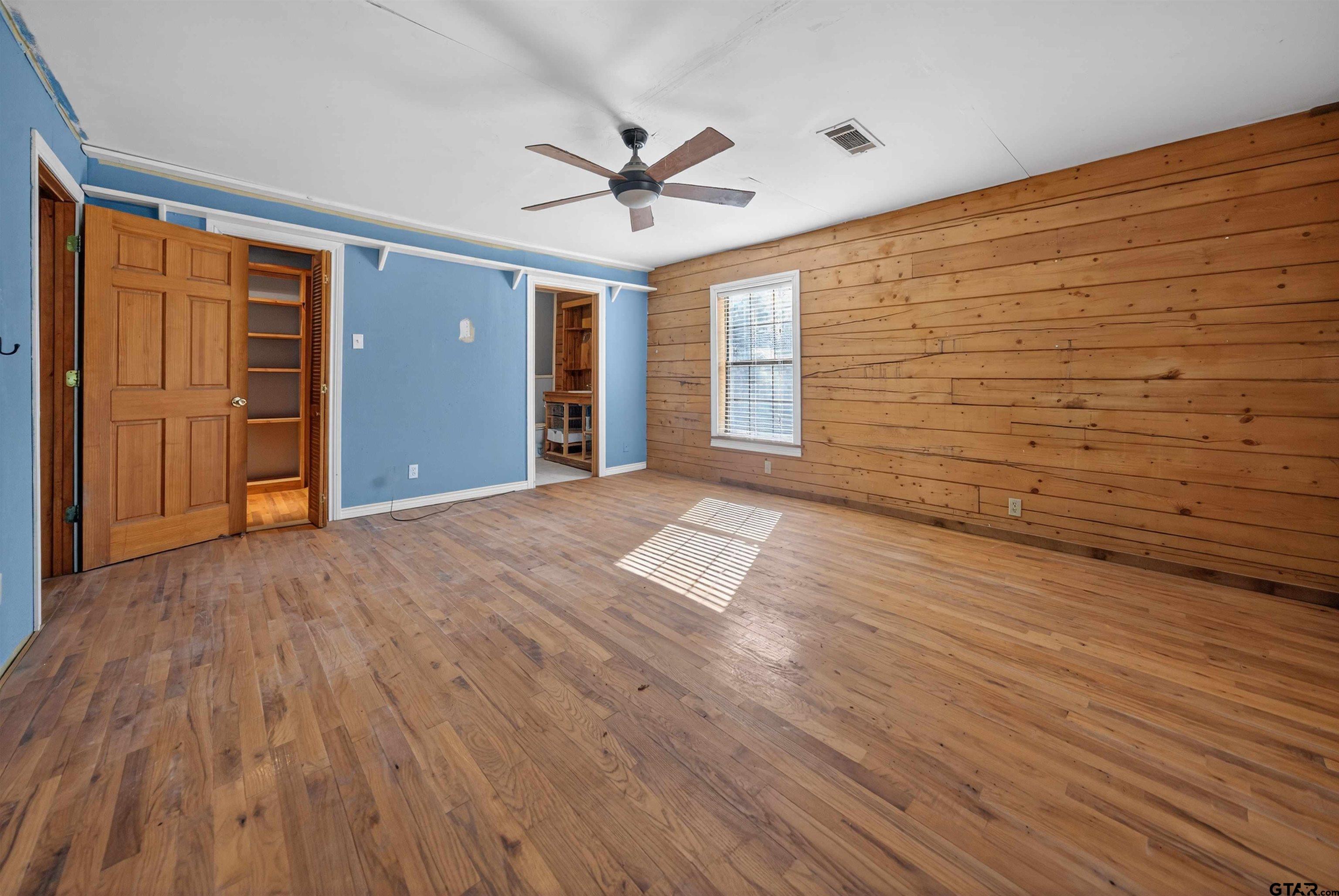 Empty bedroom with hardwood floors, a wood-plank accent wall, and a ceiling fan.