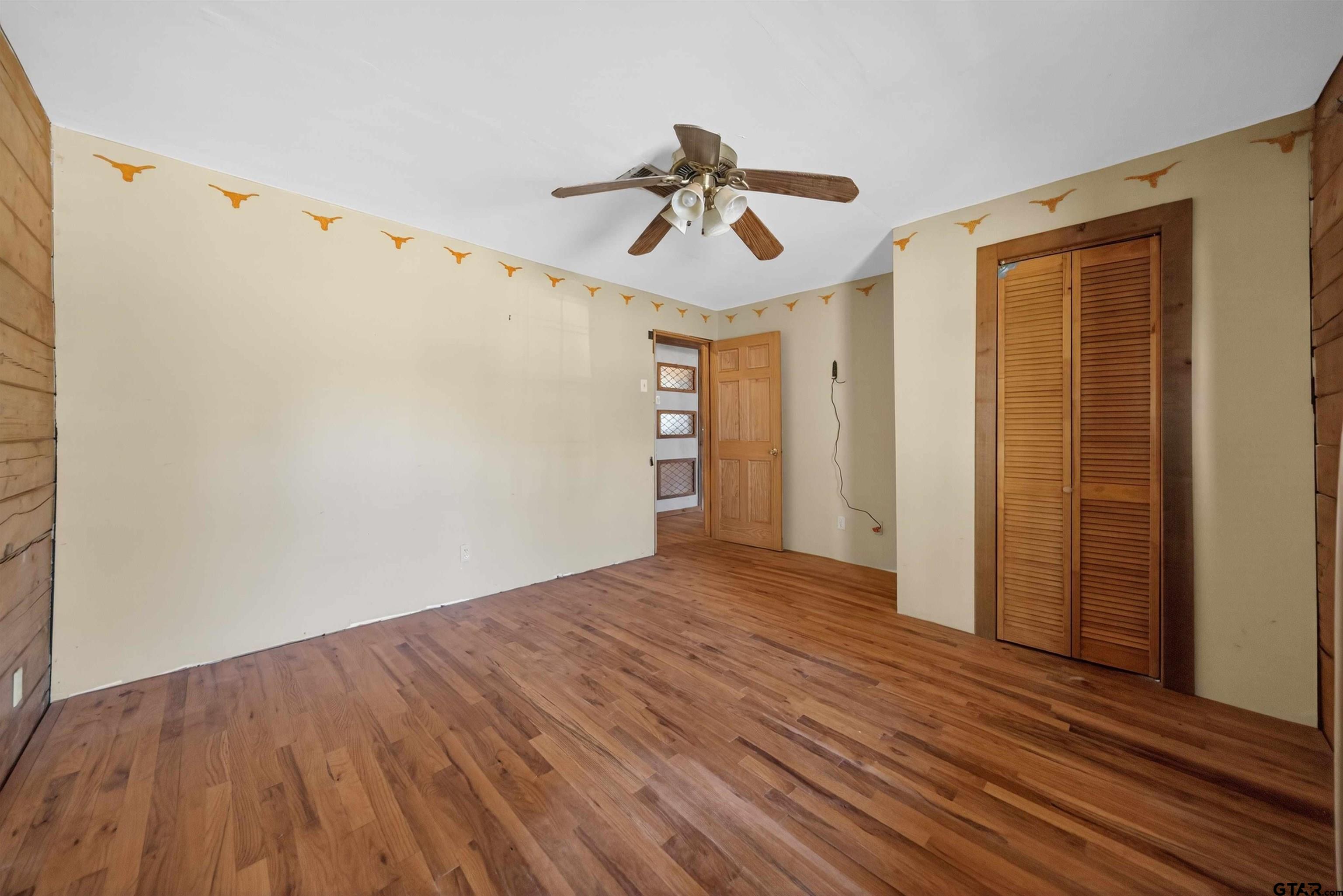 Unfurnished room with hardwood floors, a ceiling fan, louvered closet doors, and longhorn wall trim.