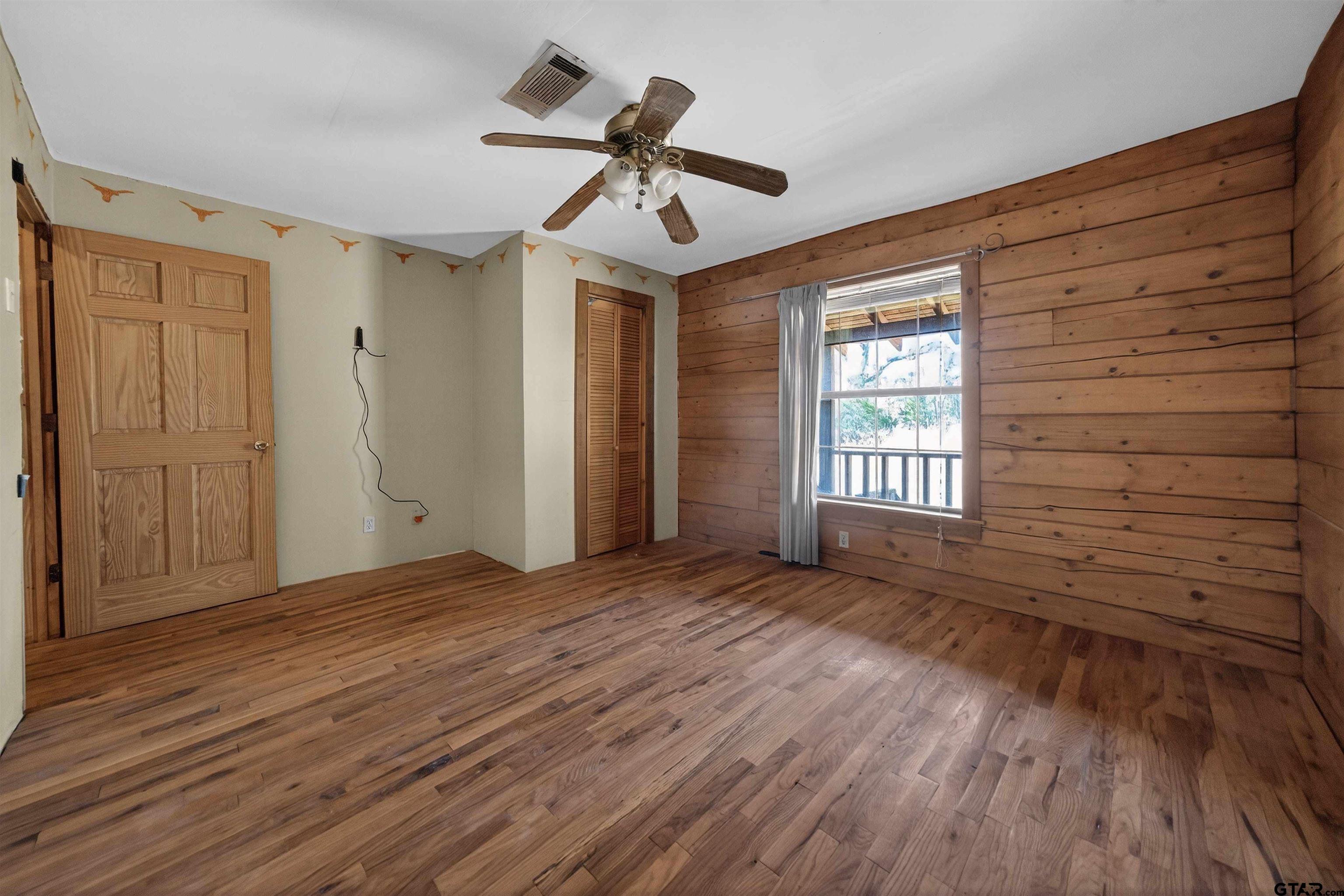 Empty bedroom with hardwood floors, a wood-plank accent wall, and a window with gray curtains.