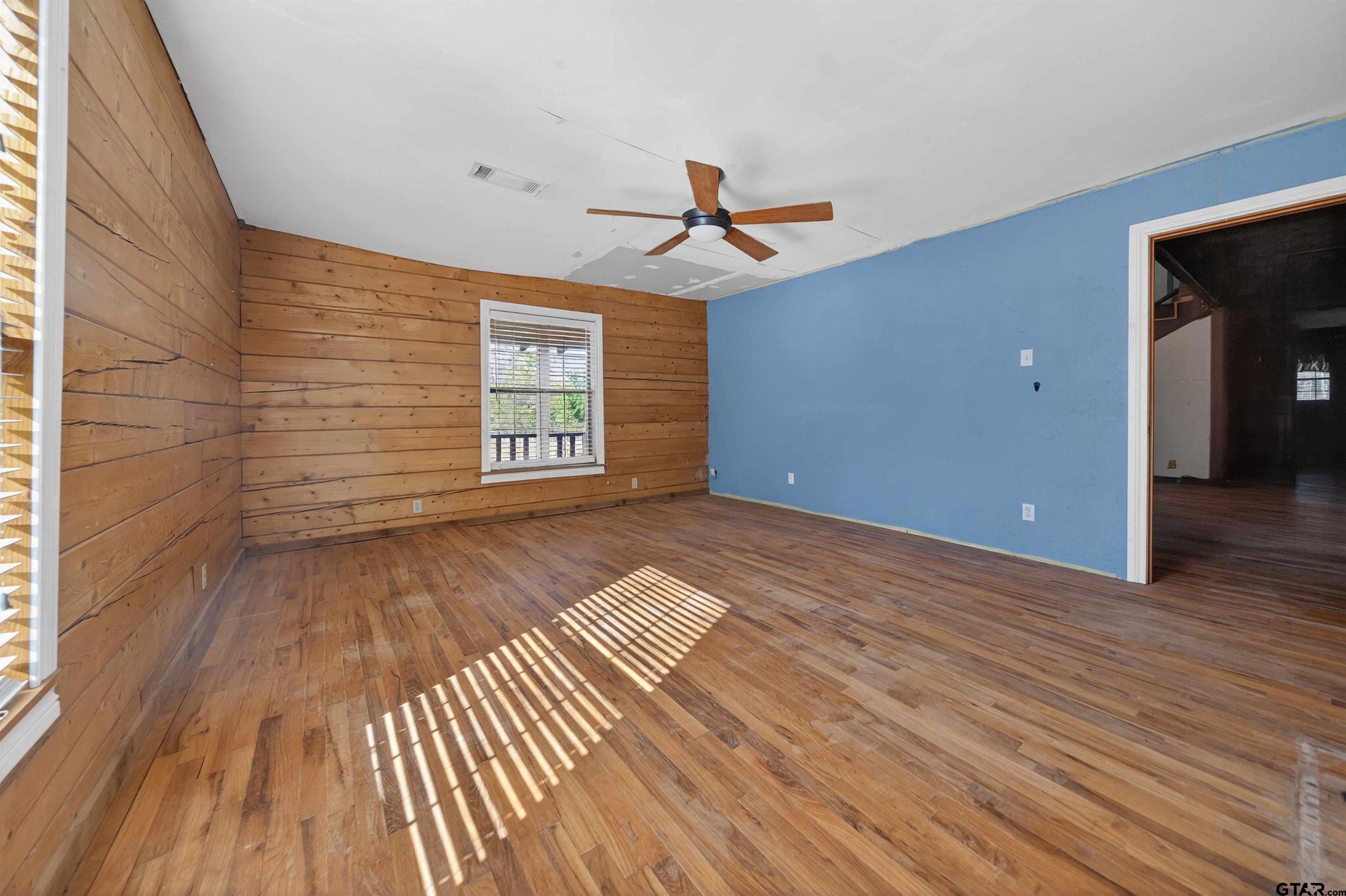 Empty room with wood floors, paneled walls, a blue wall, and sunlight stripes across the floor.