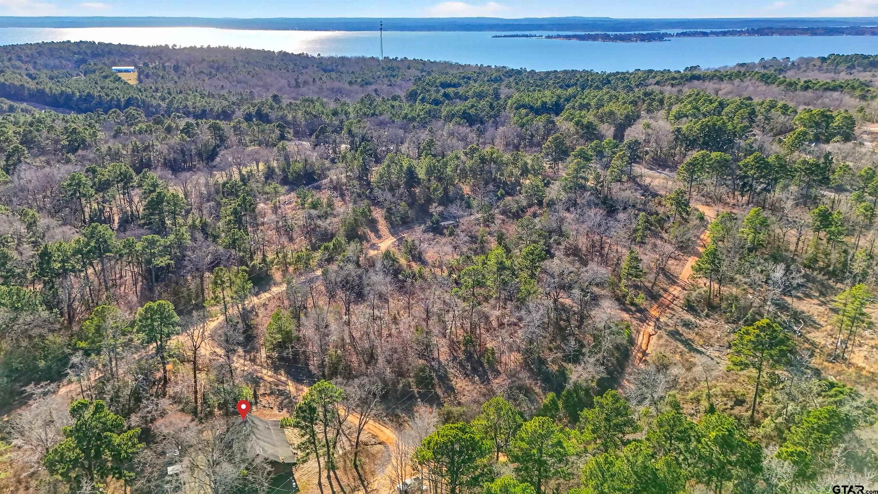 Wooded property with winding dirt roads and a lake in the distance.