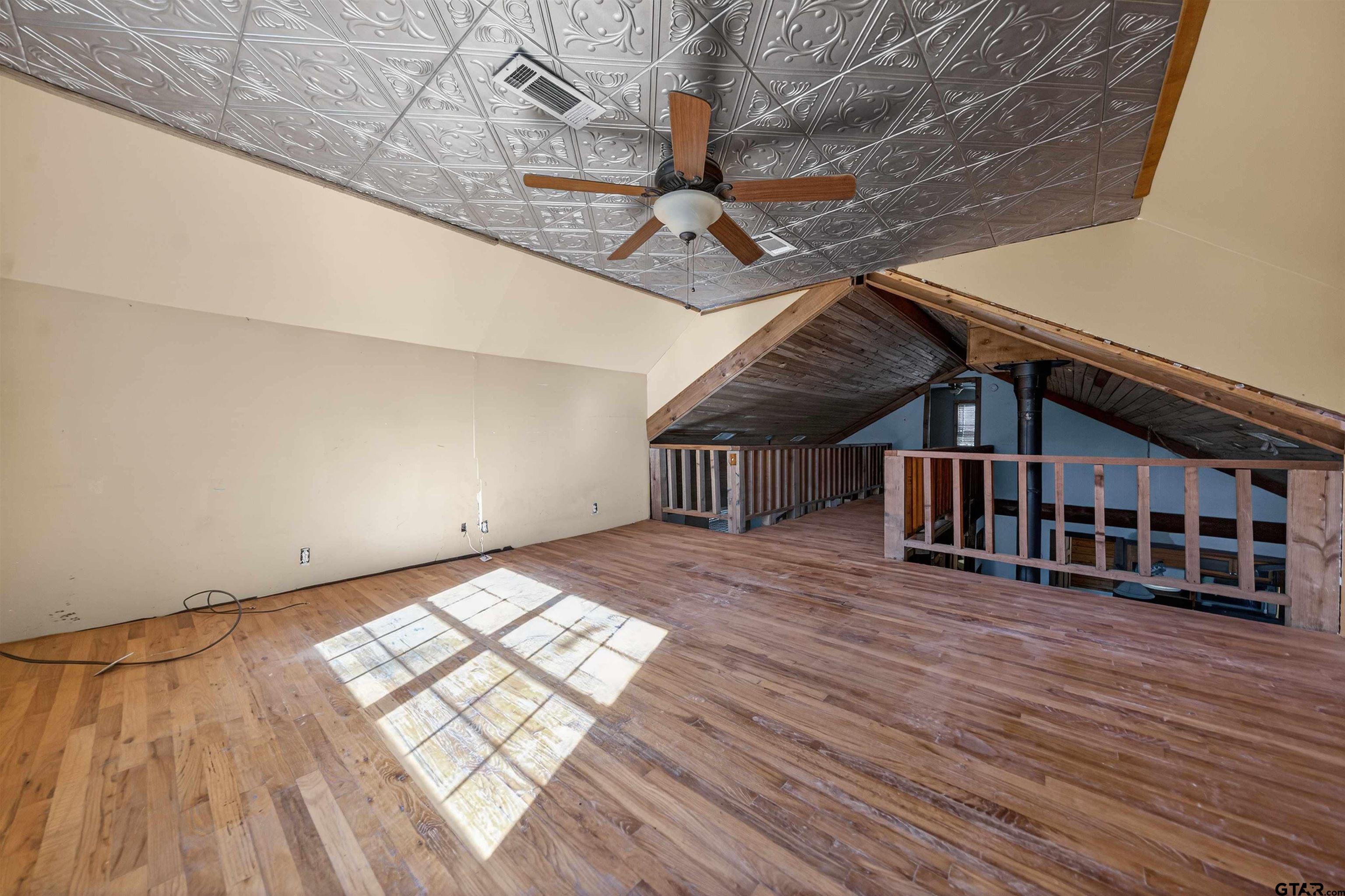 Vacant loft with wood floors, a patterned tin ceiling, and a timber railing overlooking the level below.