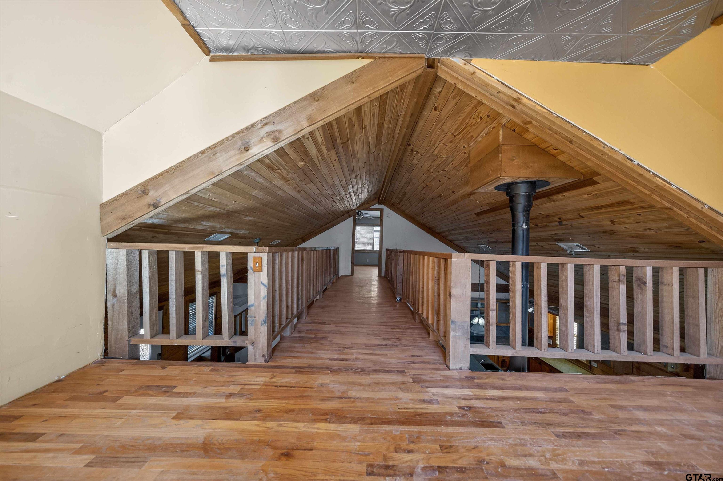 Vacant loft with a wood-floored walkway, exposed beams, and a steep wood-paneled ceiling.