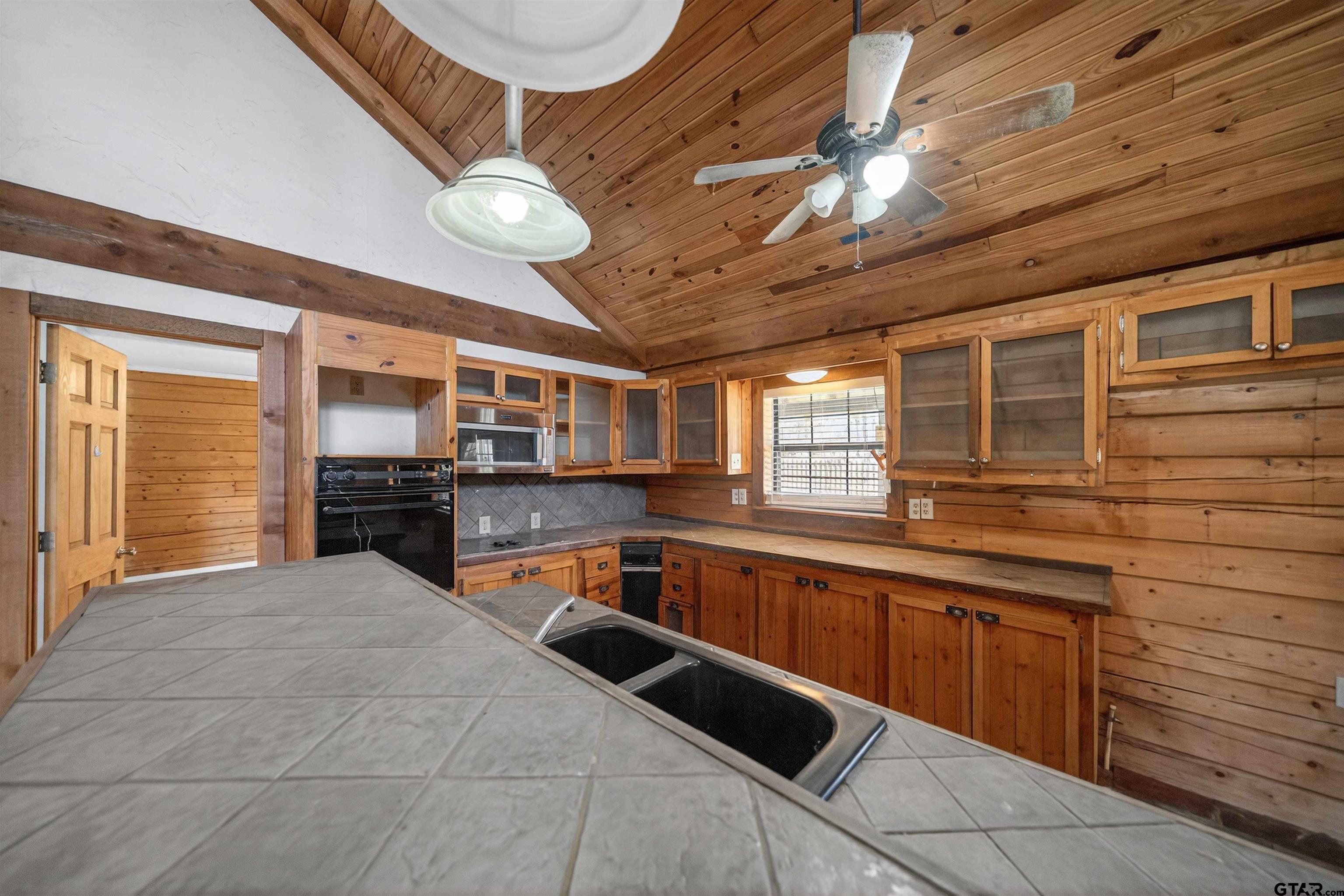 Kitchen with wood cabinetry, vaulted wood ceiling, and a large tiled island with double sink.