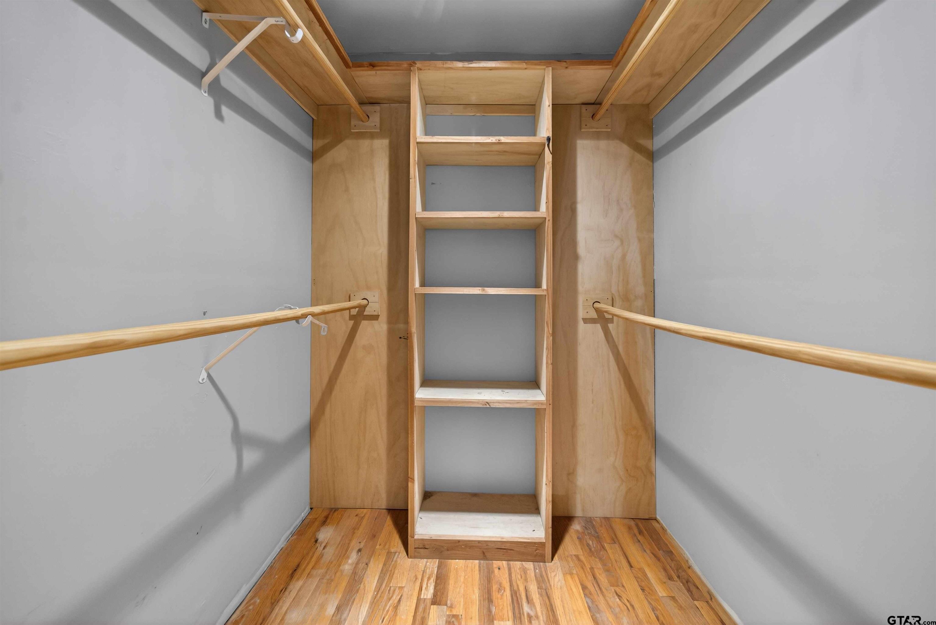 Empty walk-in closet with built-in wooden shelving, hanging rods, and wood flooring.