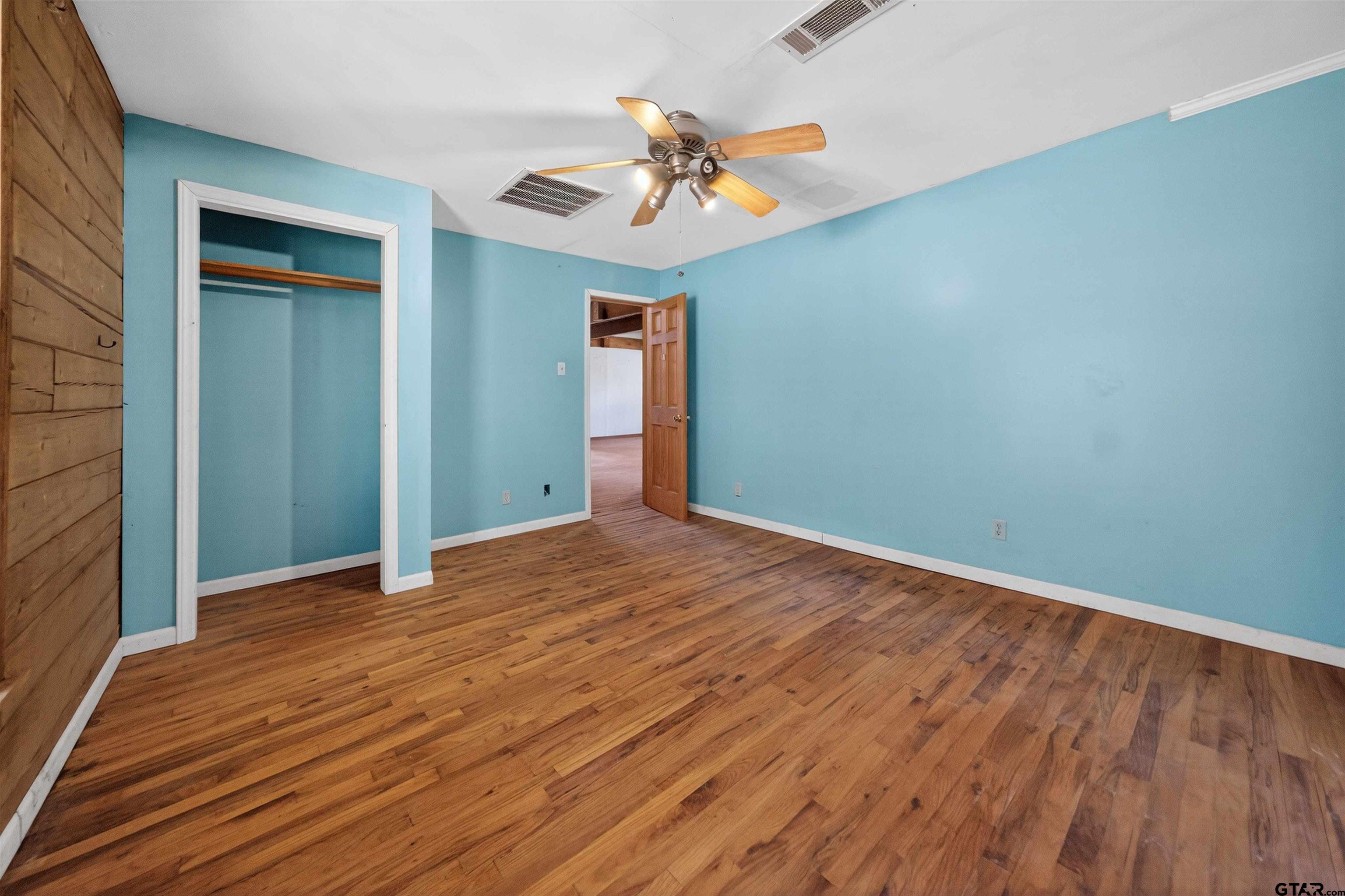 Vacant bedroom with turquoise walls, hardwood floors, and an open closet.