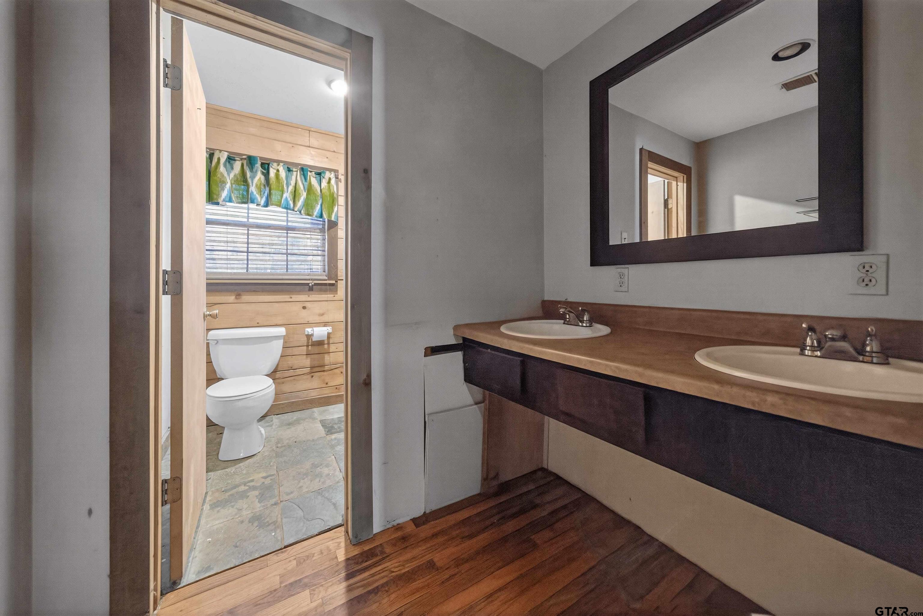 Bathroom with a double-sink wood vanity and a separate wood-paneled toilet alcove.