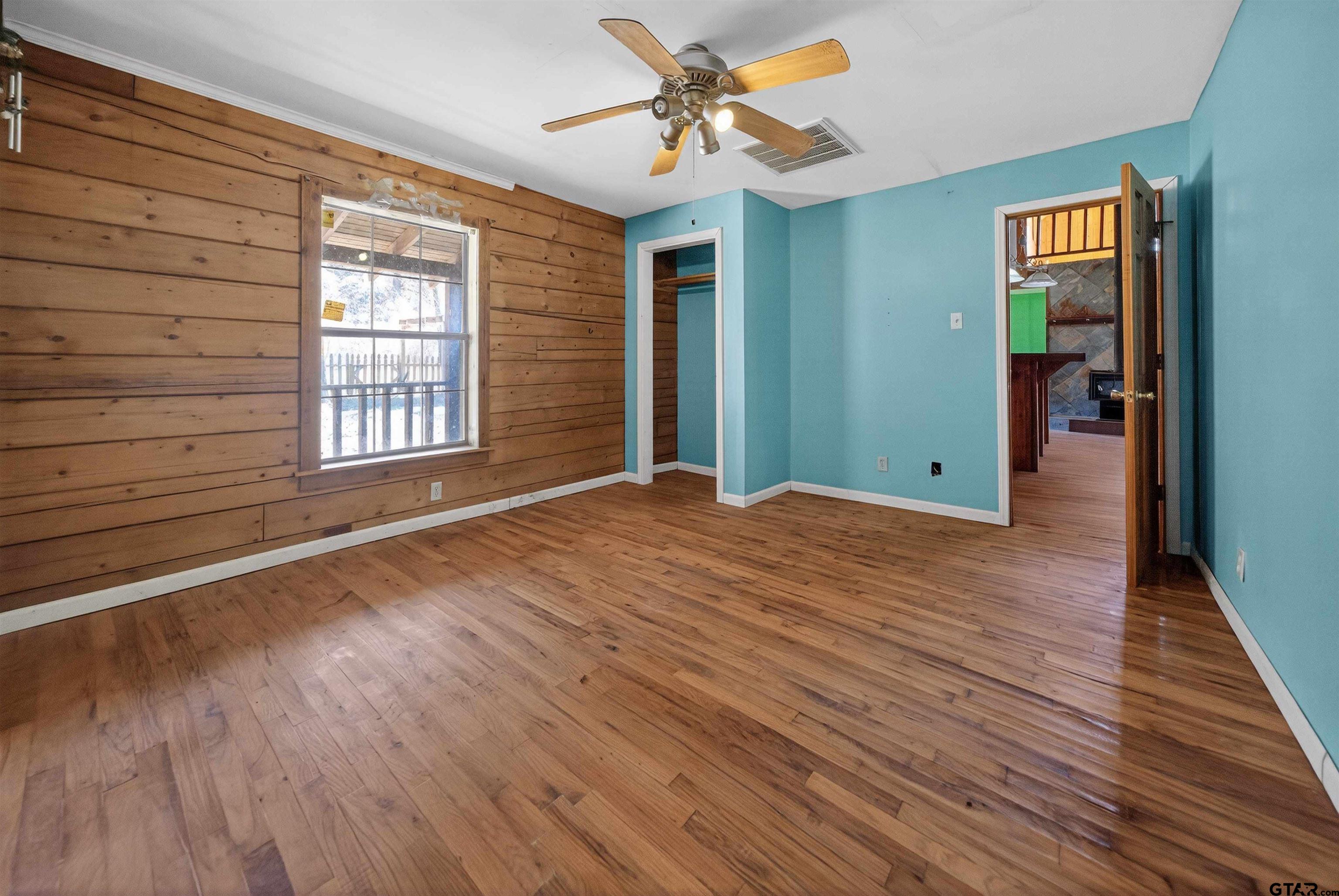 Empty room with hardwood floors, a wood-plank wall, turquoise walls, and a ceiling fan.